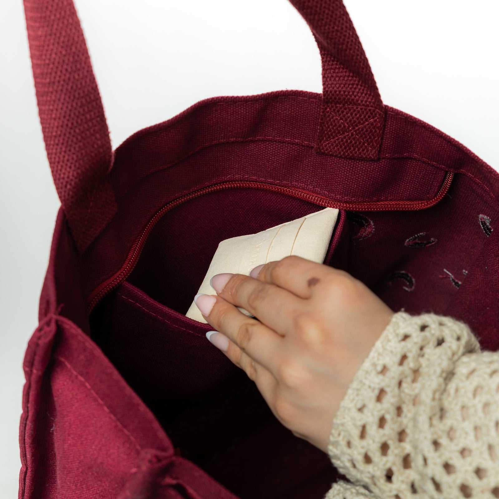Hand reaching into the bag’s interior pocket to pull out a cream-colored pouch. The inside is fully lined and features a secure pocket.