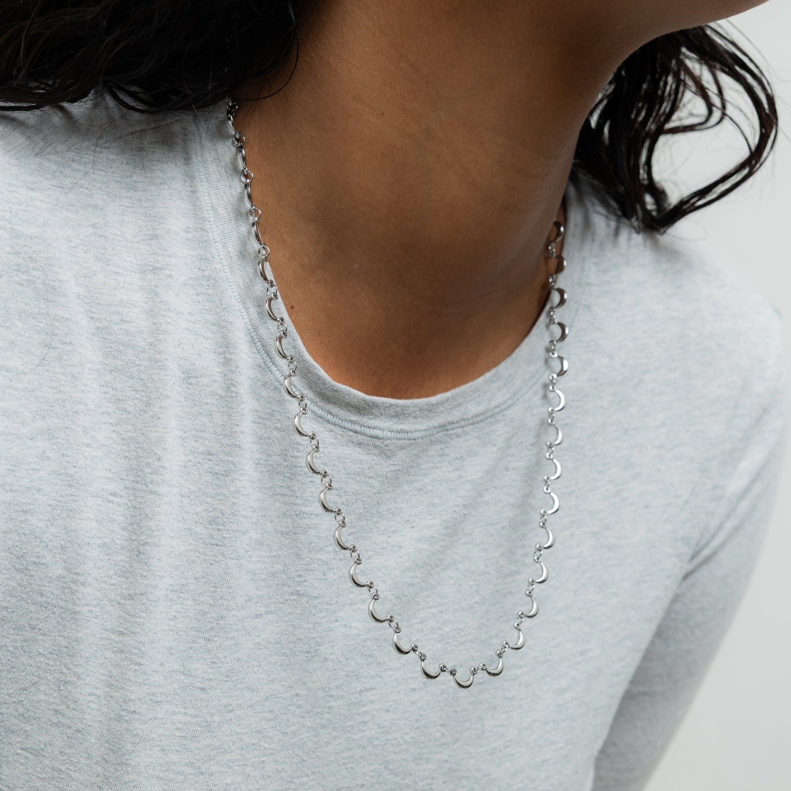 A model showcasing the silver Skyfall Necklace. The crescent-shaped charms lay gracefully on her neckline, highlighting the necklace's celestial design.