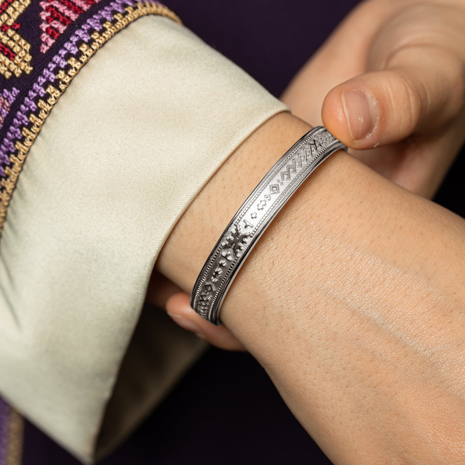 Model wearing the silver cuff on one hand while holding it with the other hand showing the design of the silver cuff.