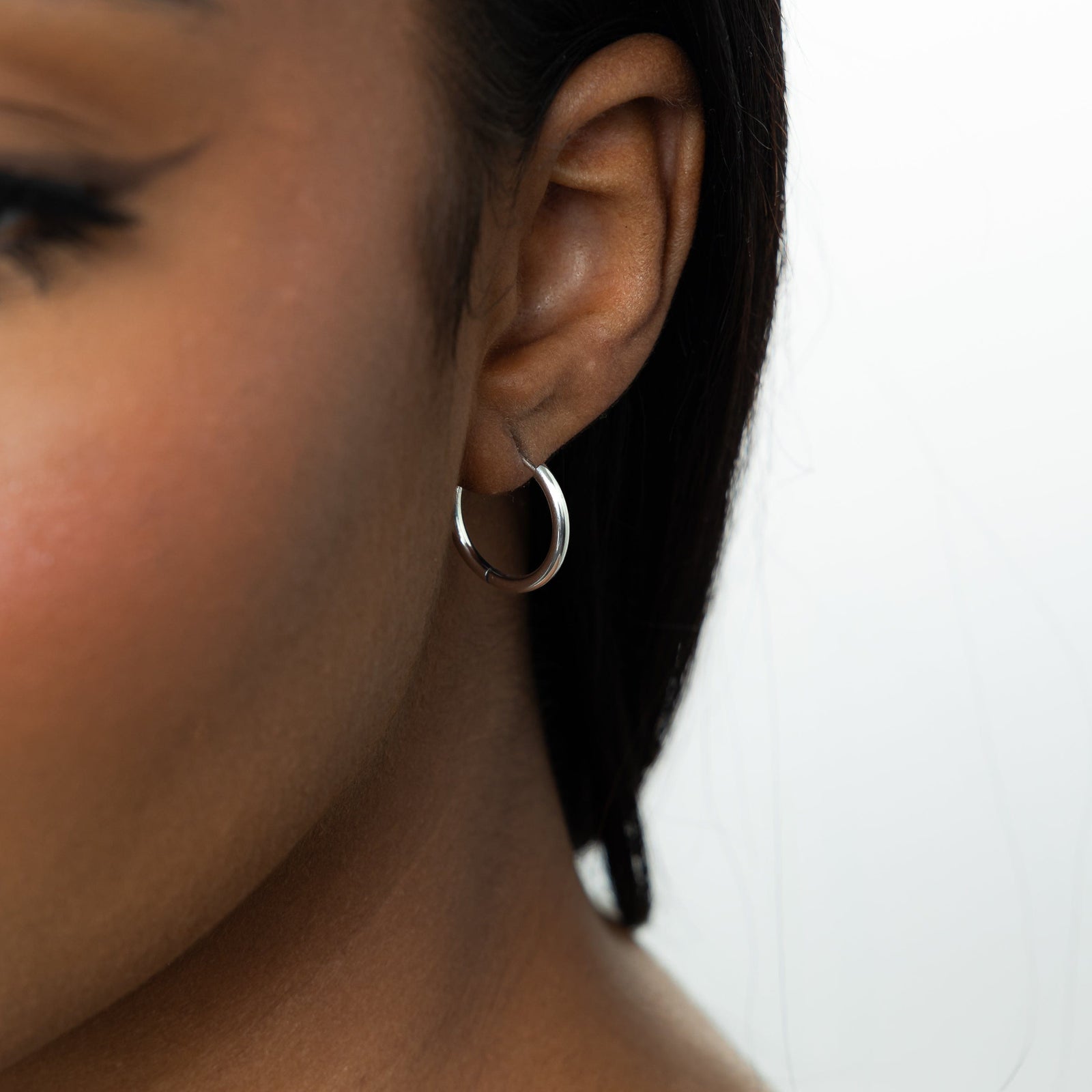 Close up of the silver Small Essential Hoops | 14mm as worn by the model on their left ear.