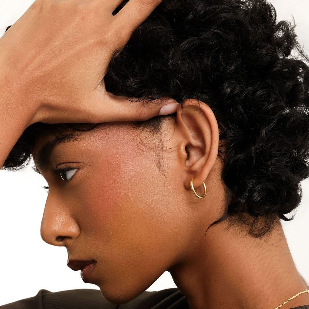 Photo of the left side profile of the model's face. The model is wearing the Small Essential Hoops | 14mm on their left ear.