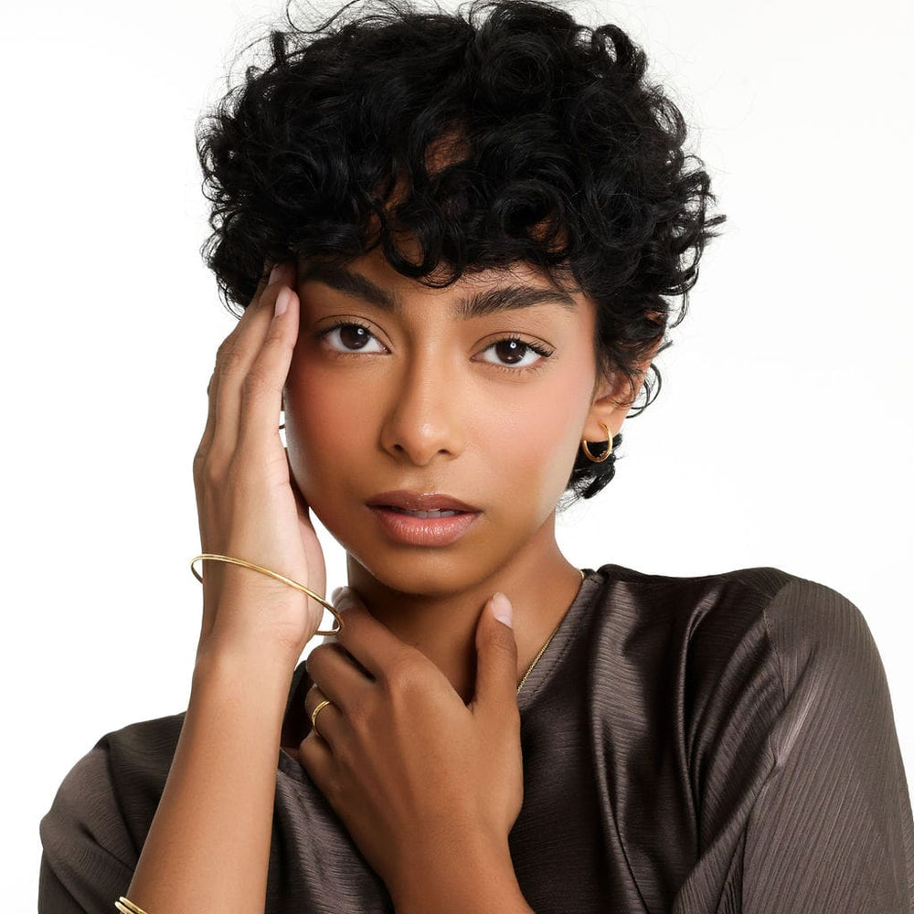 Photo of the model touching their temple and neck. The model is model is wearing a few accessories one of them is the Small Essential Hoops | 14mm