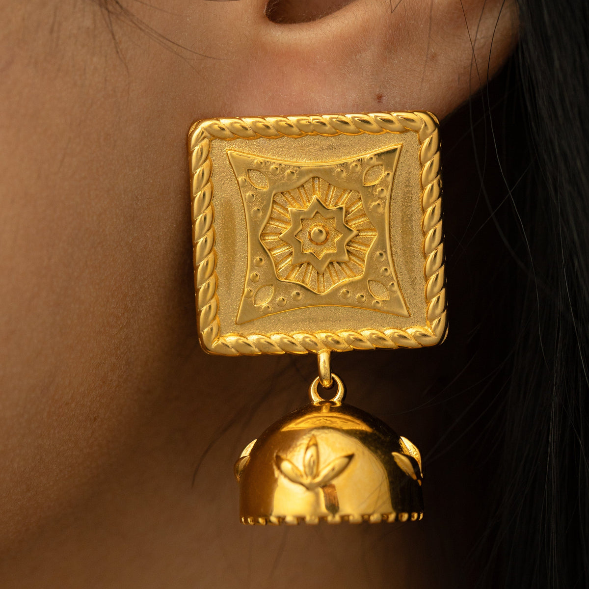 Close-up of a woman wearing the gold Square Jhumka Earring, showcasing the engraved square top with floral detailing and dangling dome jhumka with leaf motifs.