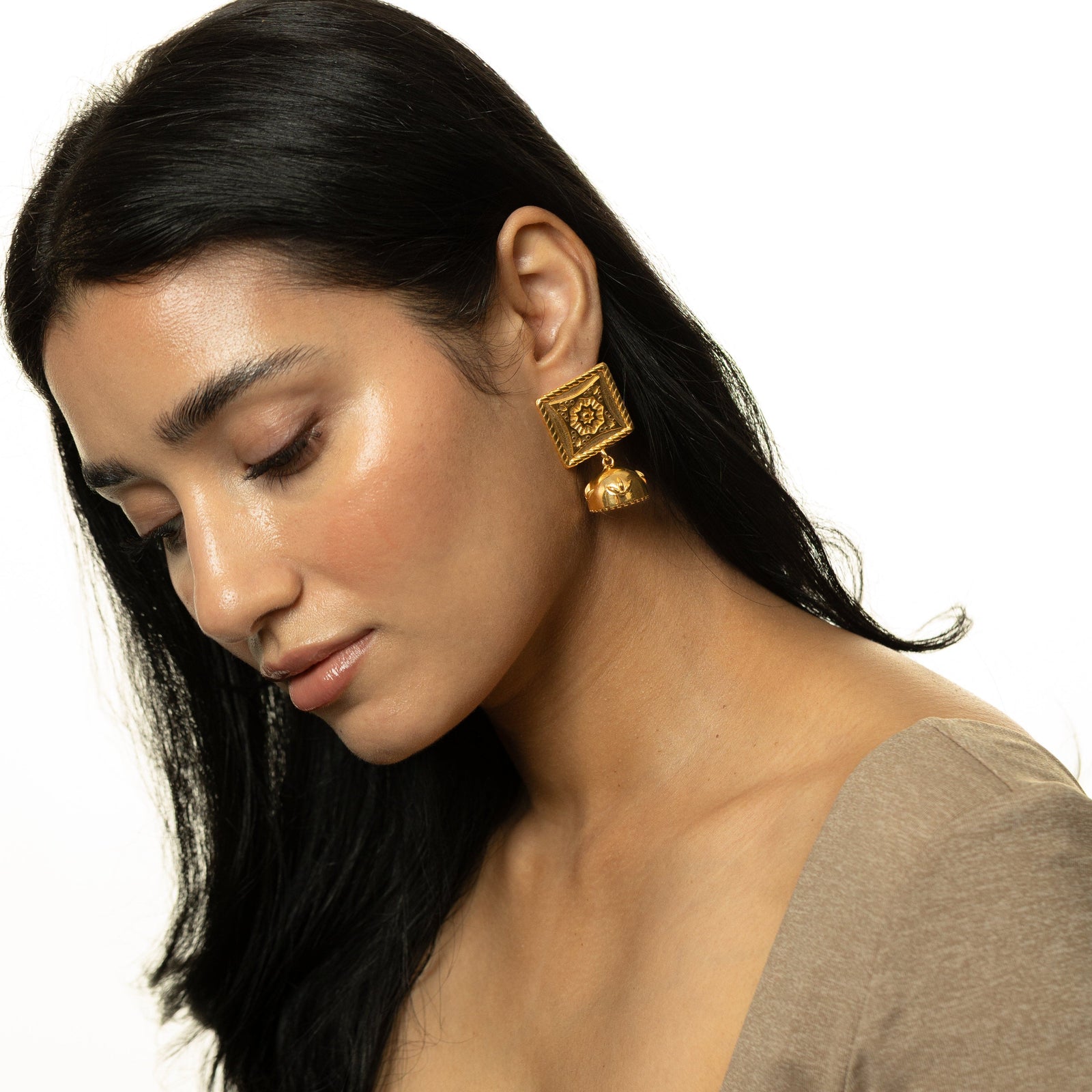 Woman looking downward, wearing the gold Square Jhumka Earrings with engraved square tops and dome-shaped jhumkas, styled with a beige top.