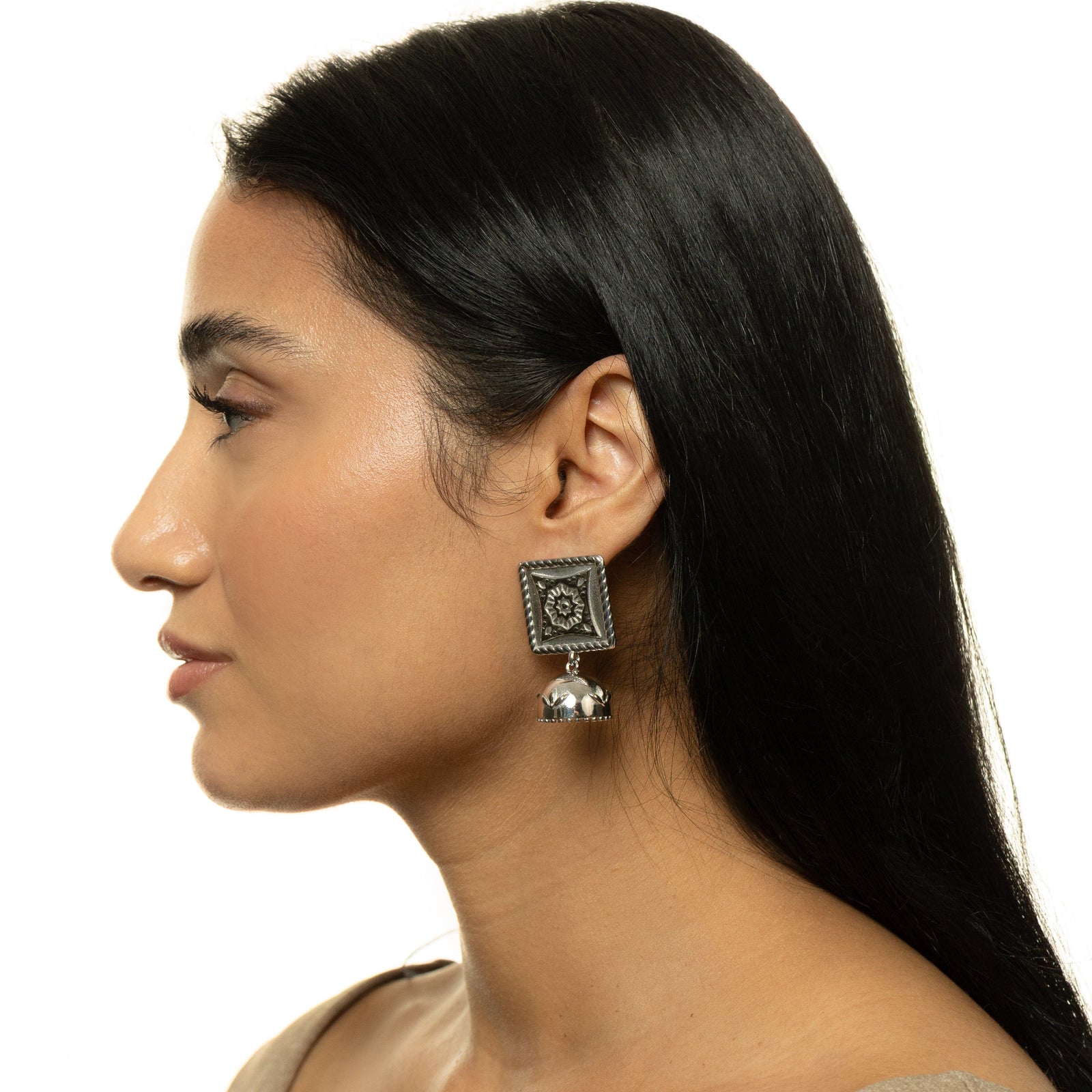 A woman wearing the silver Square Jhumka Earring, styled with long dark hair tucked back to reveal the engraved square and dangling dome jhumka design.