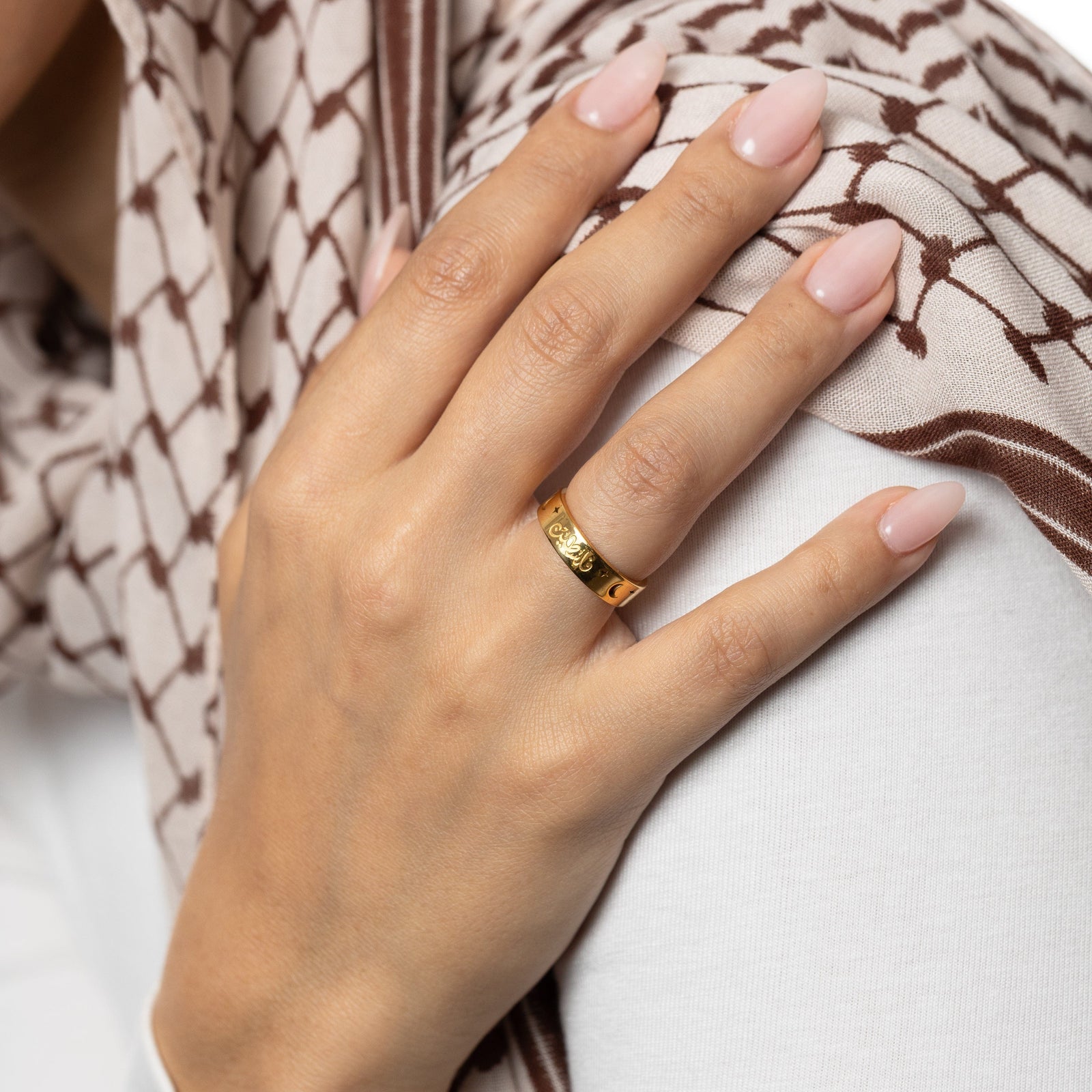 Hand wearing a gold palestine ring. Hand resting on a keffiyeh patterned fabric.