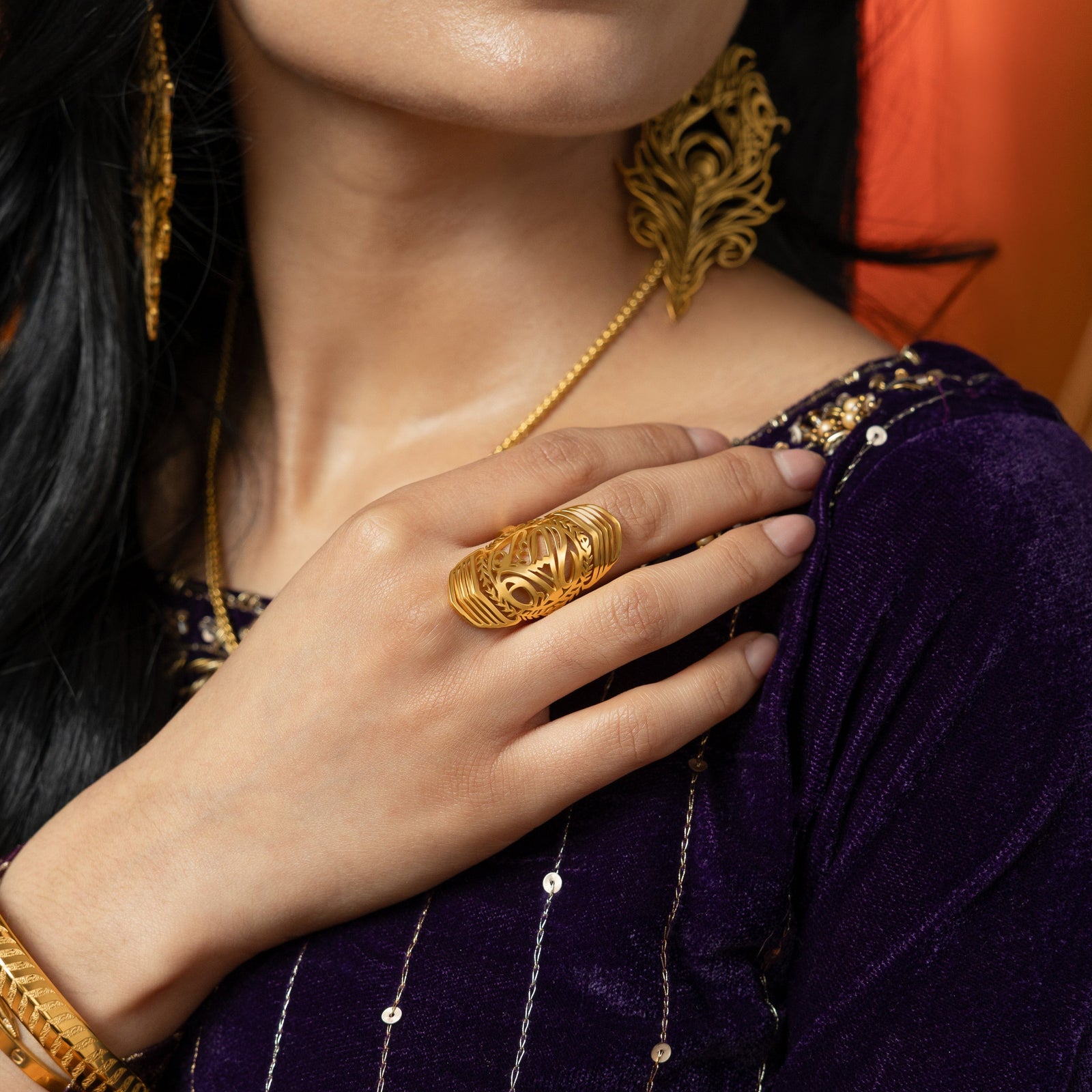 Woman wearing the gold sufficient  ring on her finger, styled with a deep purple outfit.