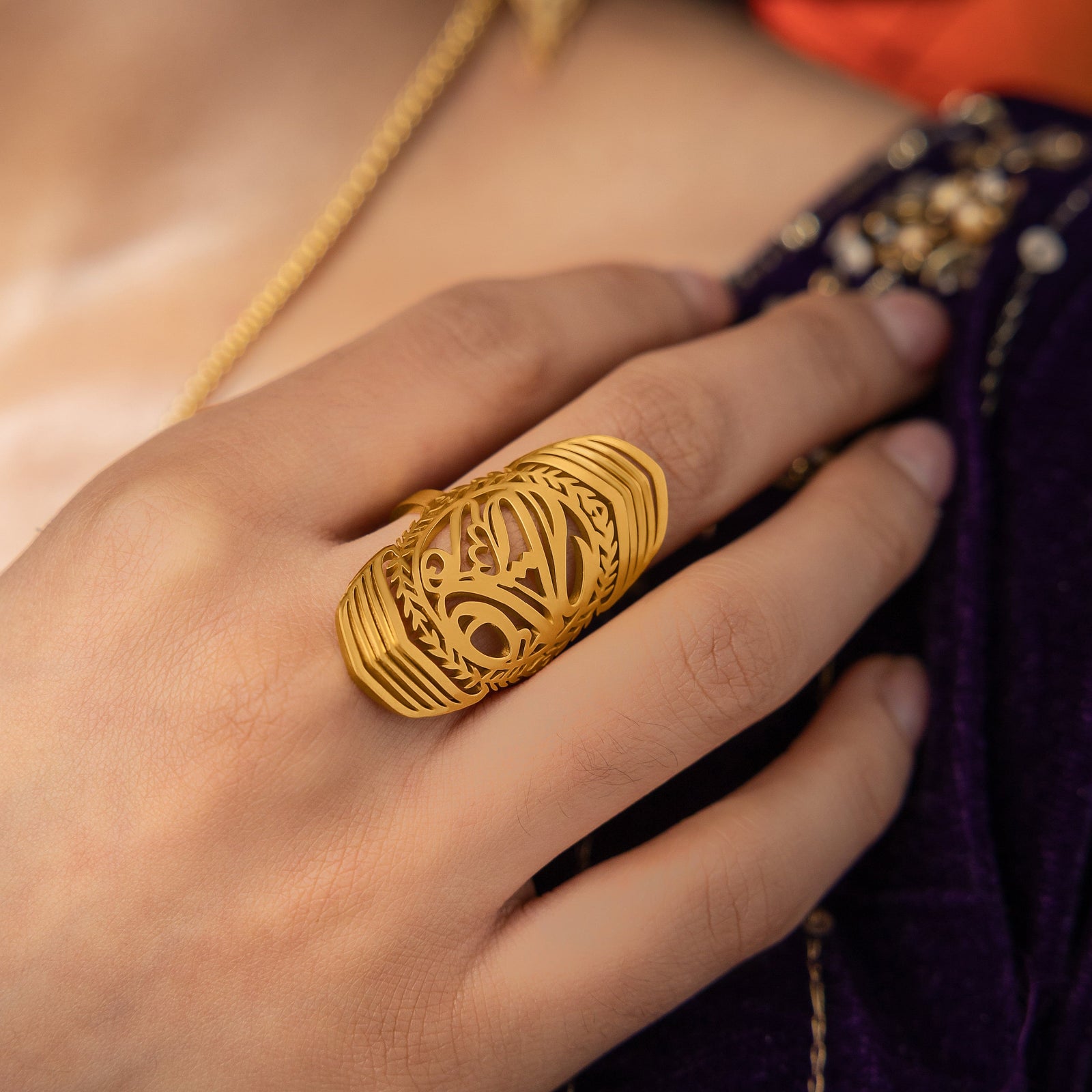Woman wearing the gold sufficient  ring on her finger, styled with a deep purple outfit.