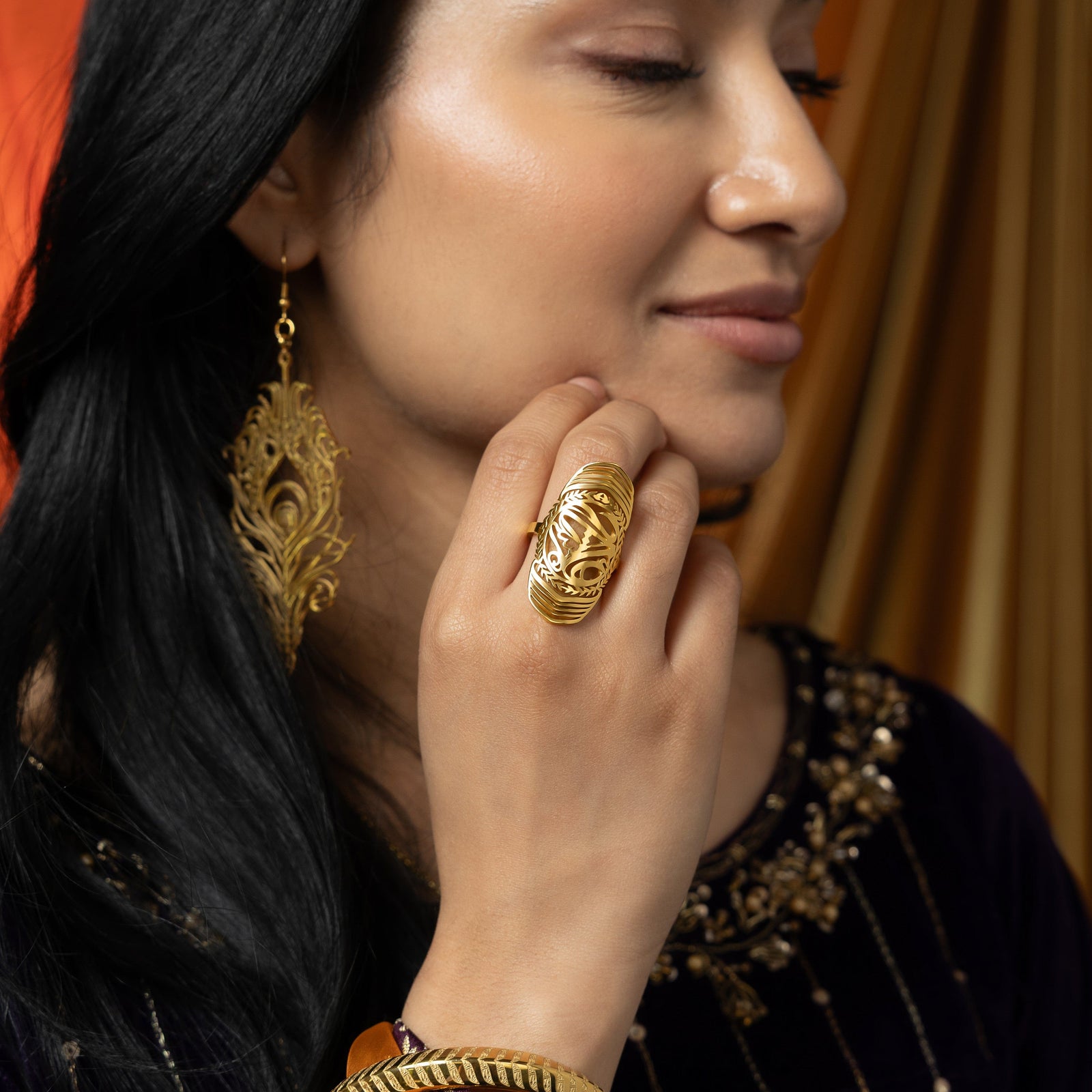 Woman wearing the gold sufficient  ring on her finger, styled with a deep purple outfit.