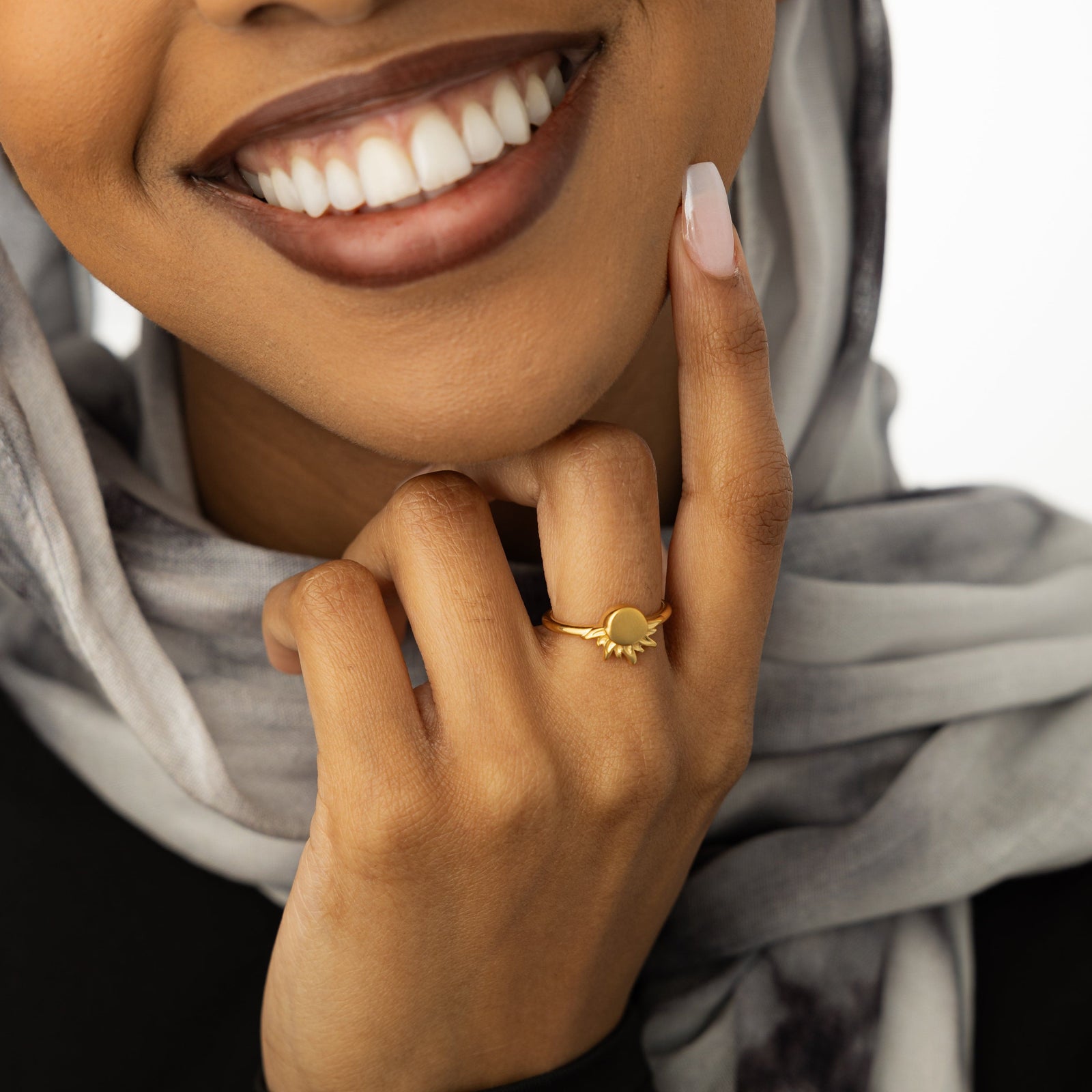 Womanwearing a gold sun ring, styled with a light patterned scarf