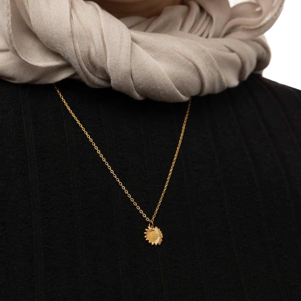 Close up of the gold Sun Flower necklace rested against the black fabric of the model's top shirt.