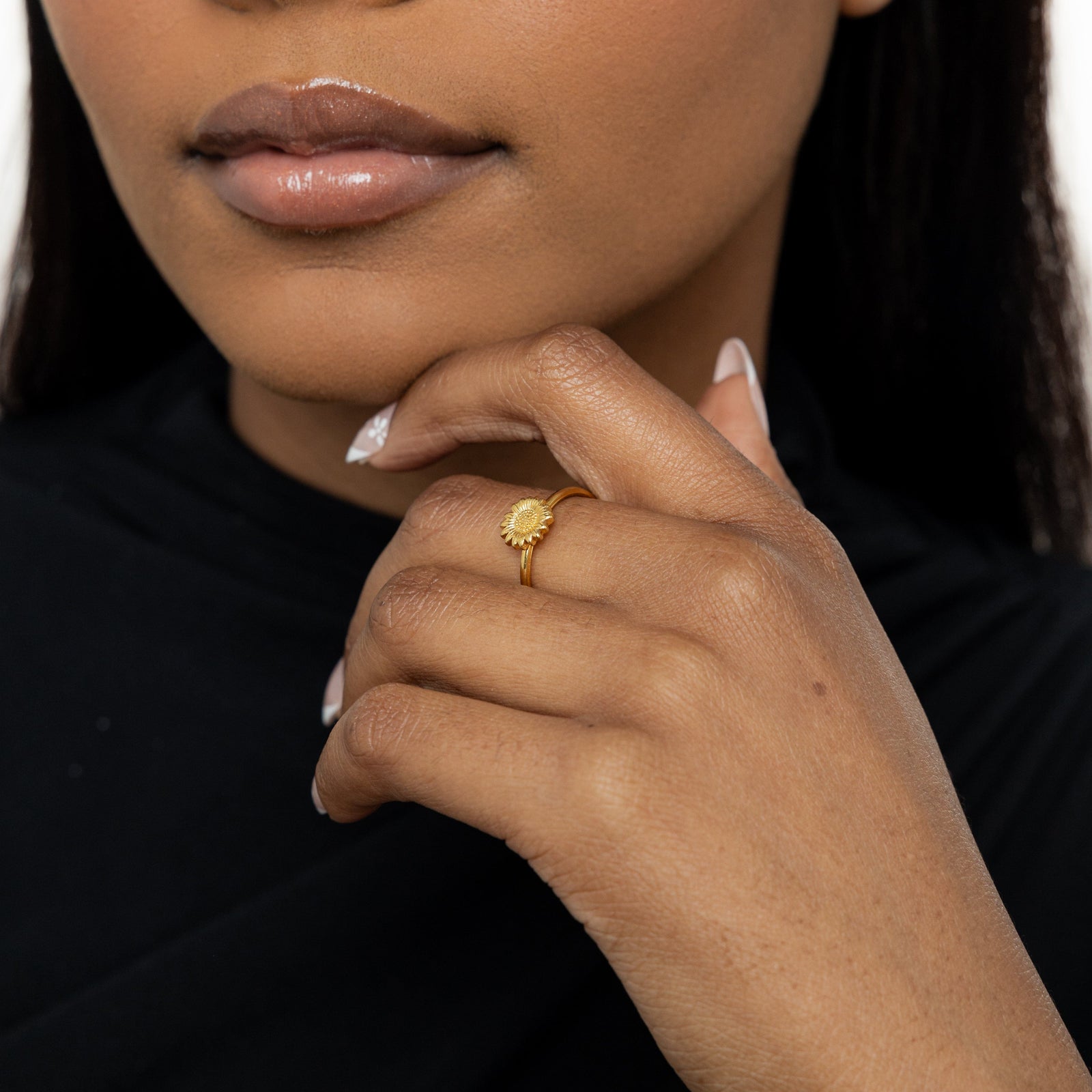 Woman wearing a gold sunflower ring, hand gently resting against her chin