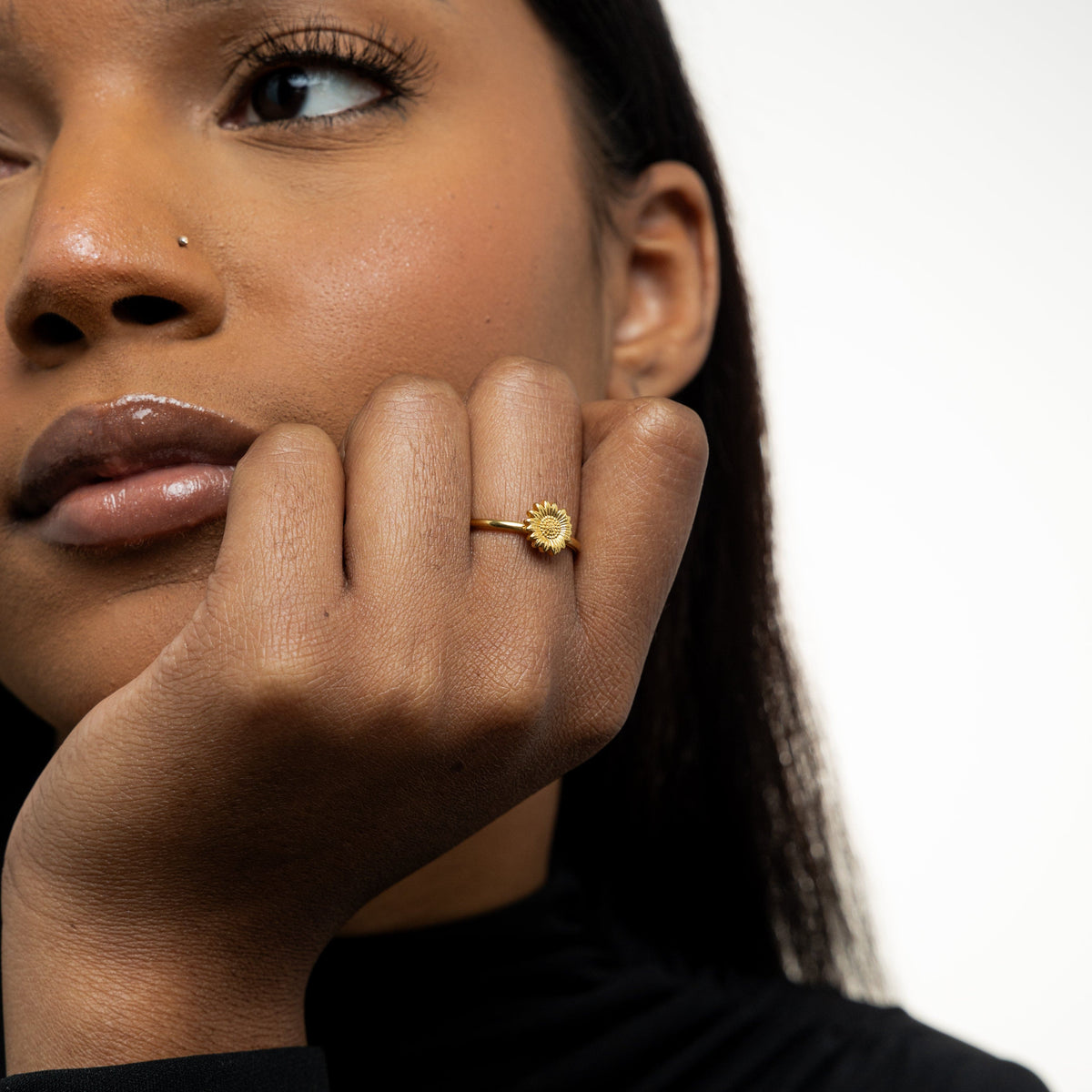 Woman wearing a gold sunflower ring on her finger, hand resting near her face.