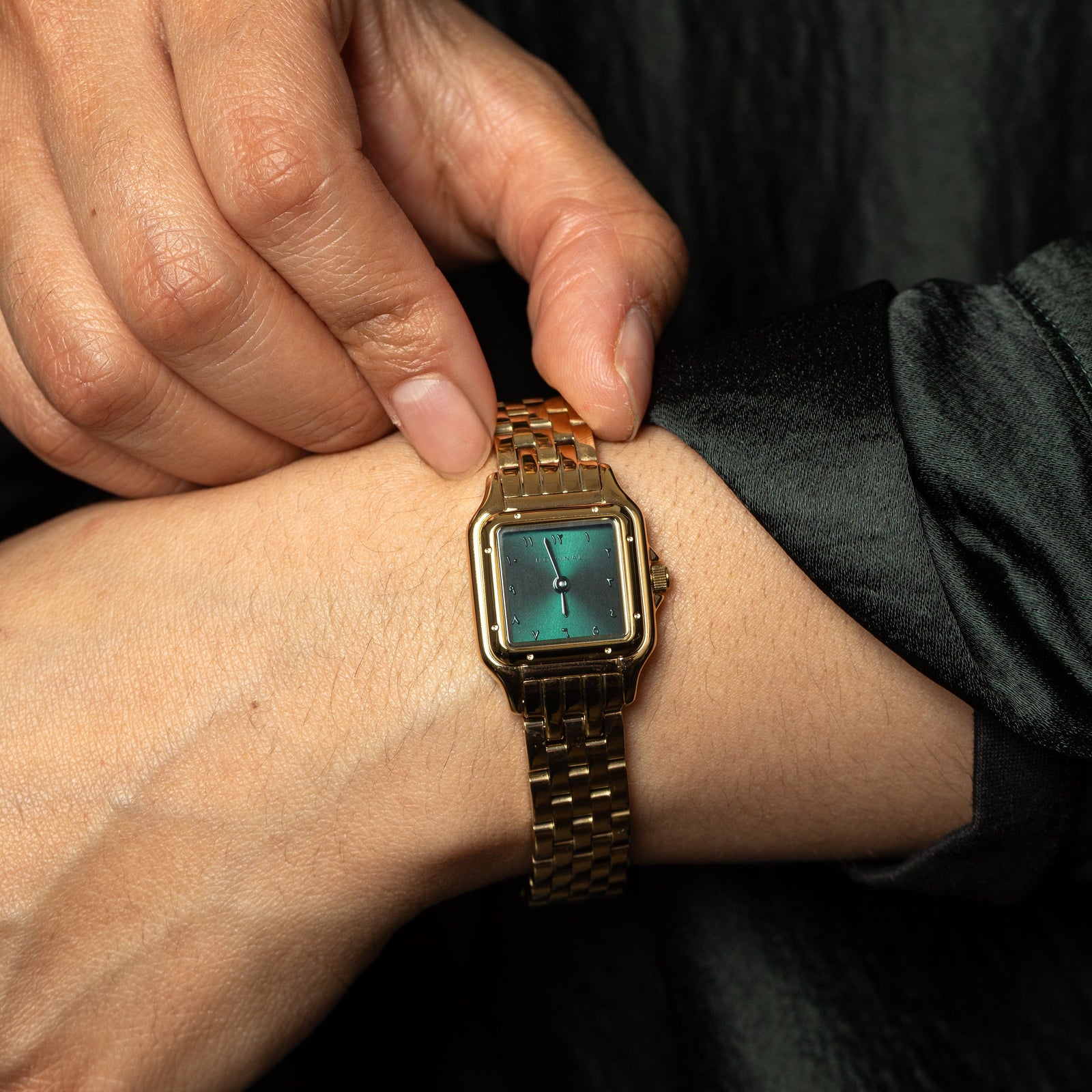 Model touching the gold watch on their wrist.