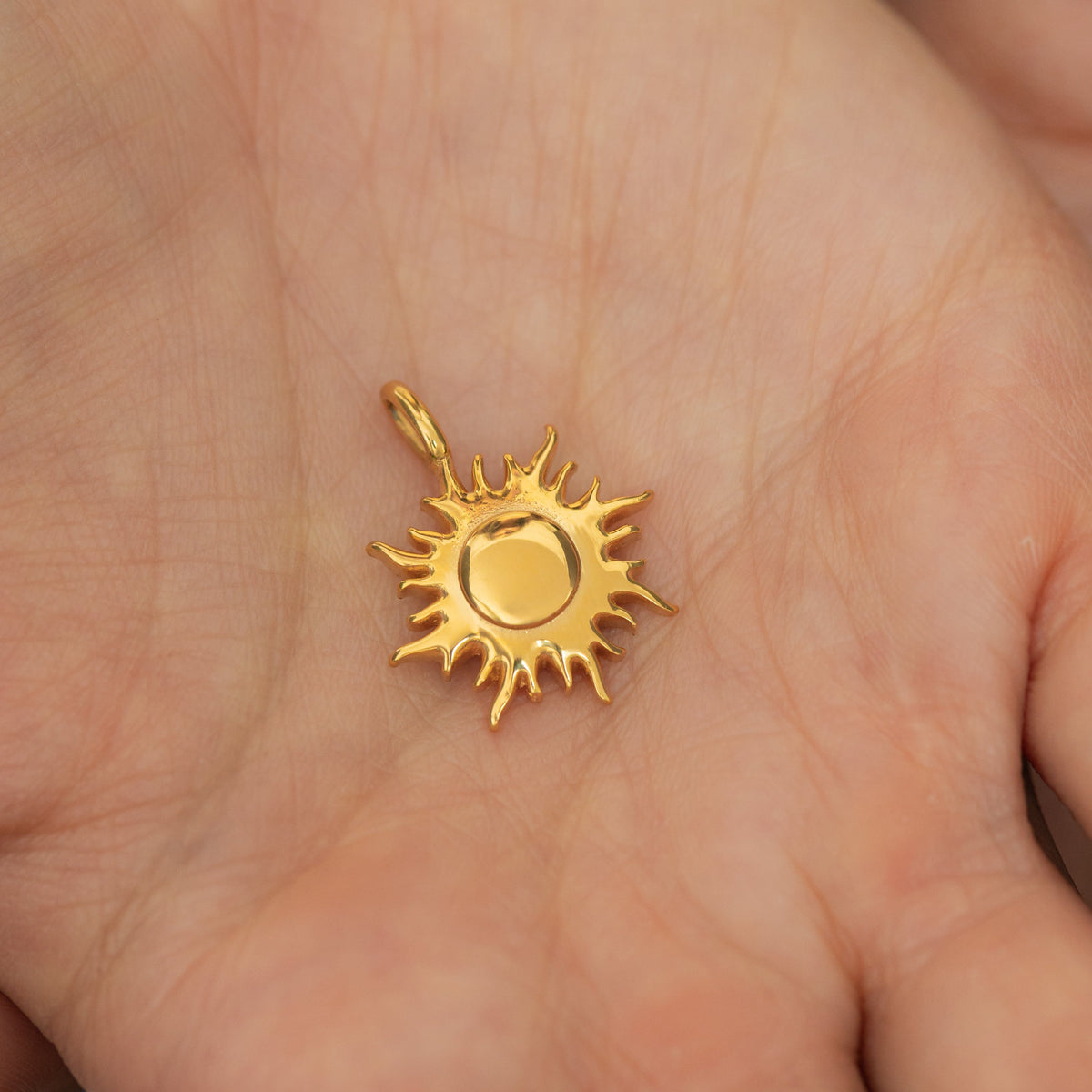 Gold sunshine charm resting on an open palm, highlighting its rays and polished center circle.