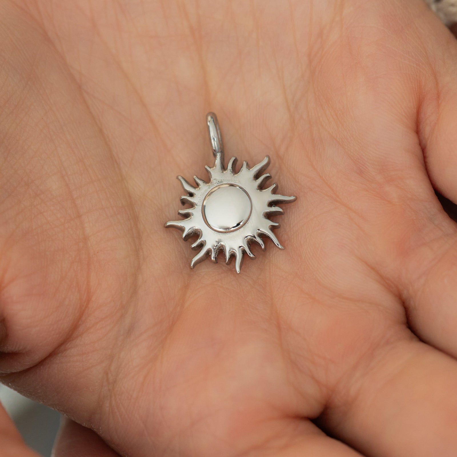 Silver sunshine charm placed on the center of a hand, showing its high-shine center and pointed ray details.