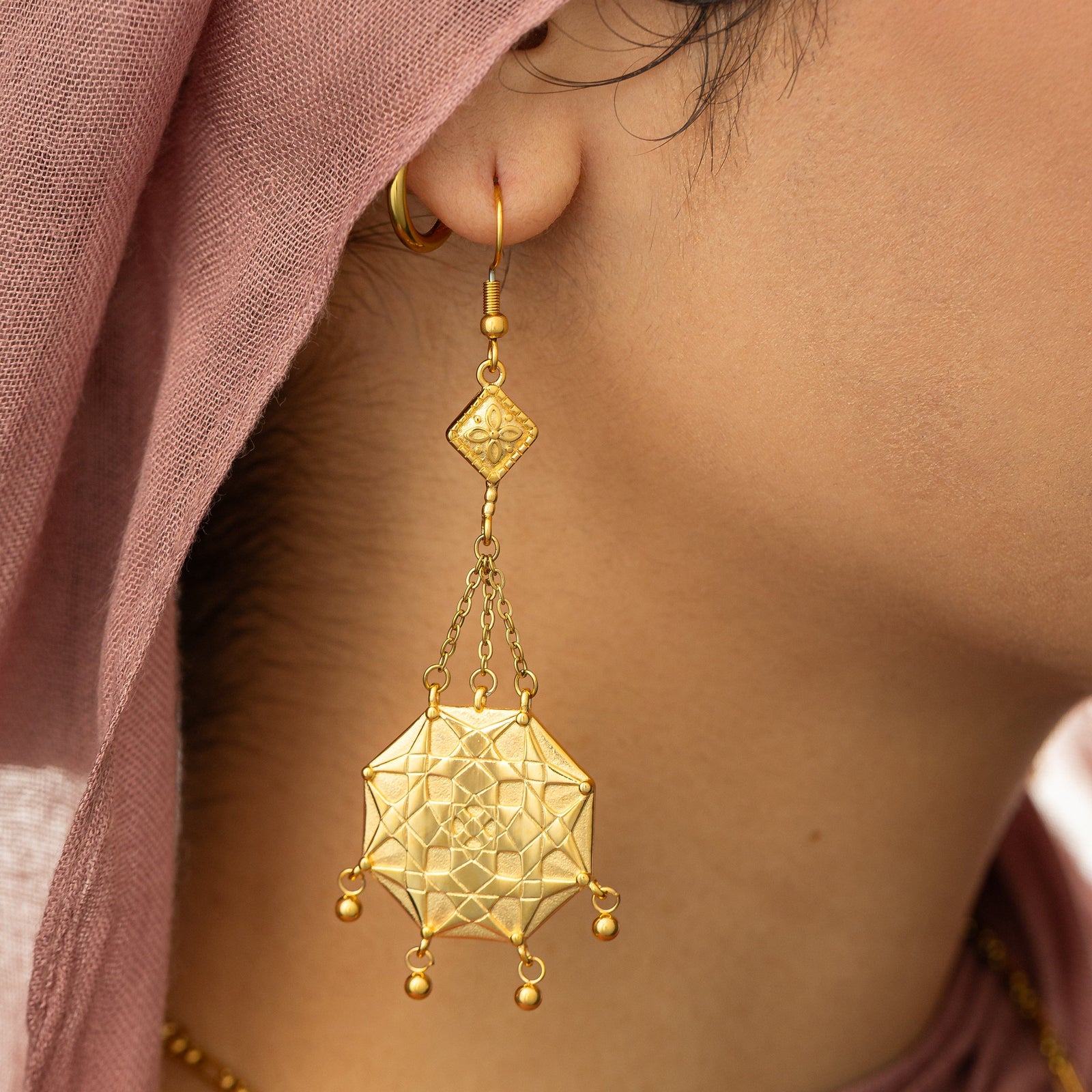 Close up photo of the gold earring focusing on the details of its design.