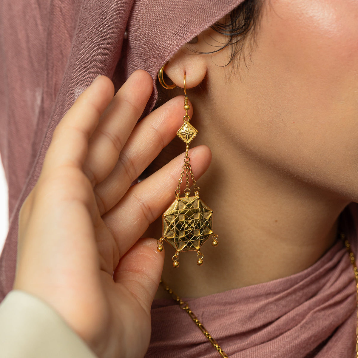 Close up photo of a model wearing and touching the gold Syrian Mosaic Earrings.