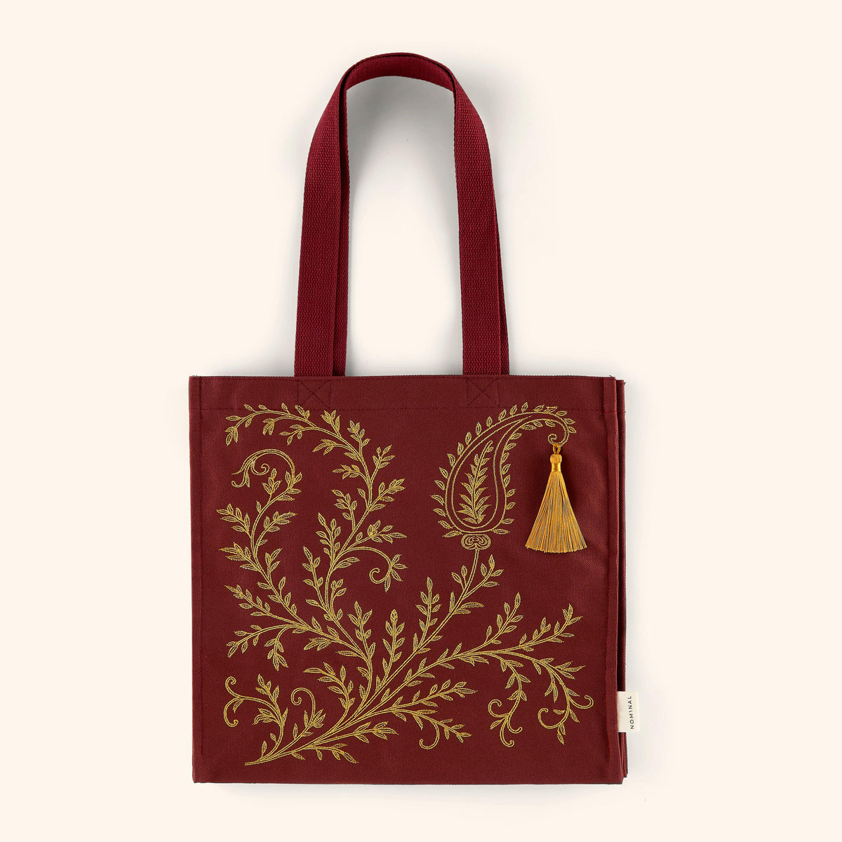 Maroon textured cotton canvass tote bag with design inspired by Mehndi patterns.  This piece swirls those patterns and comes to a Paisley pattern with a tassel 