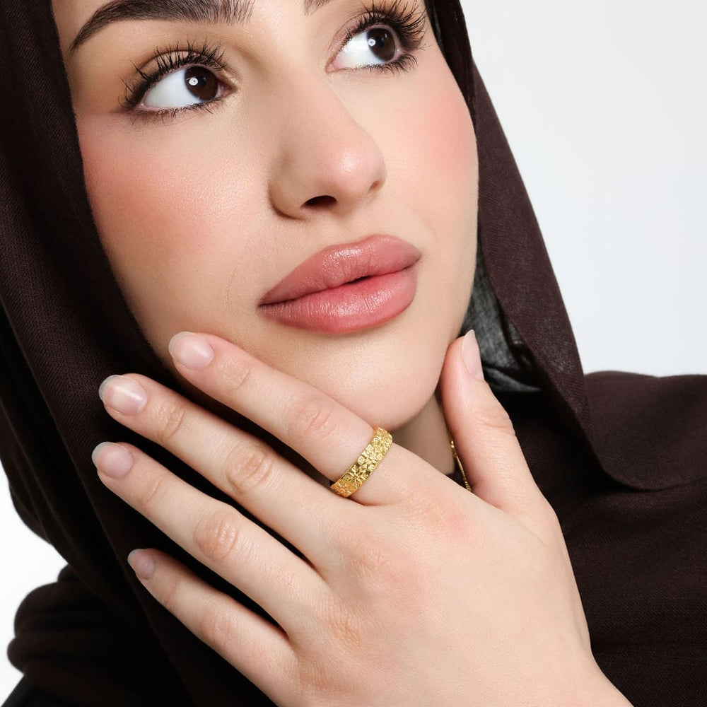 Close up of the model's face and their left hand touching their chin to show the gold Tatreez Ring on their left index finger.
