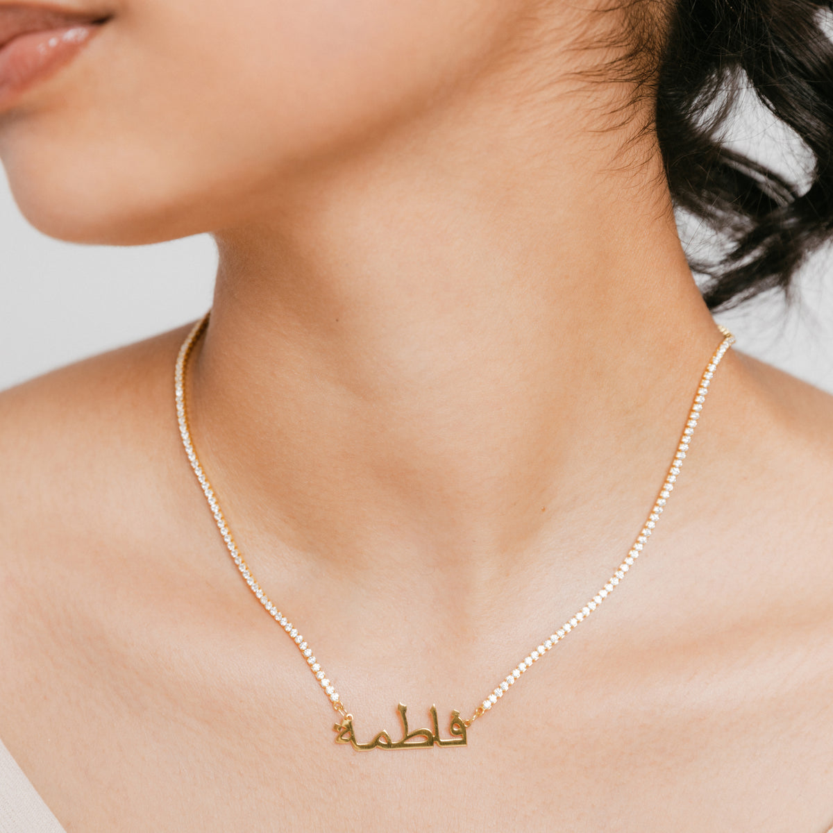 Model wearing 18k gold-plated Tennis Name Bracelet featuring a clear pavé crystal chain with a central custom Arabic calligraphy nameplate.