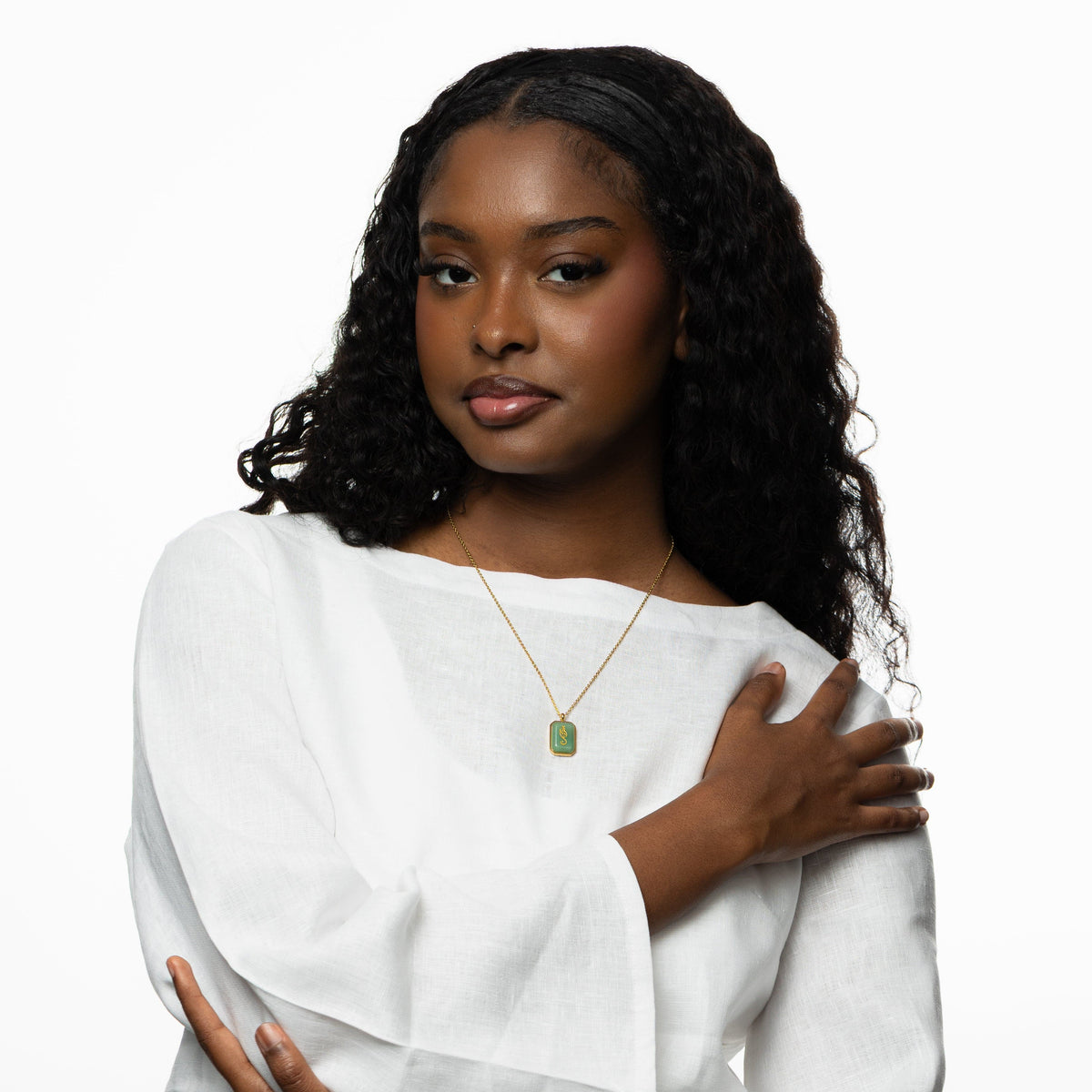 Woman wearing a gold chain necklace with a rectangular green aventurine pendant engraved with "Tawakkul" in Arabic calligraphy, styled with a white blouse.