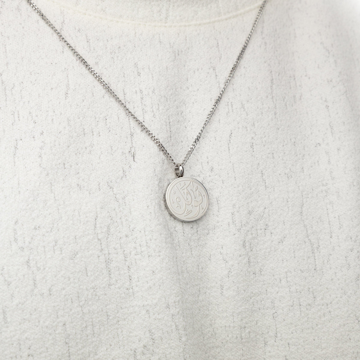 Silver trust token necklace worn on a textured white top.