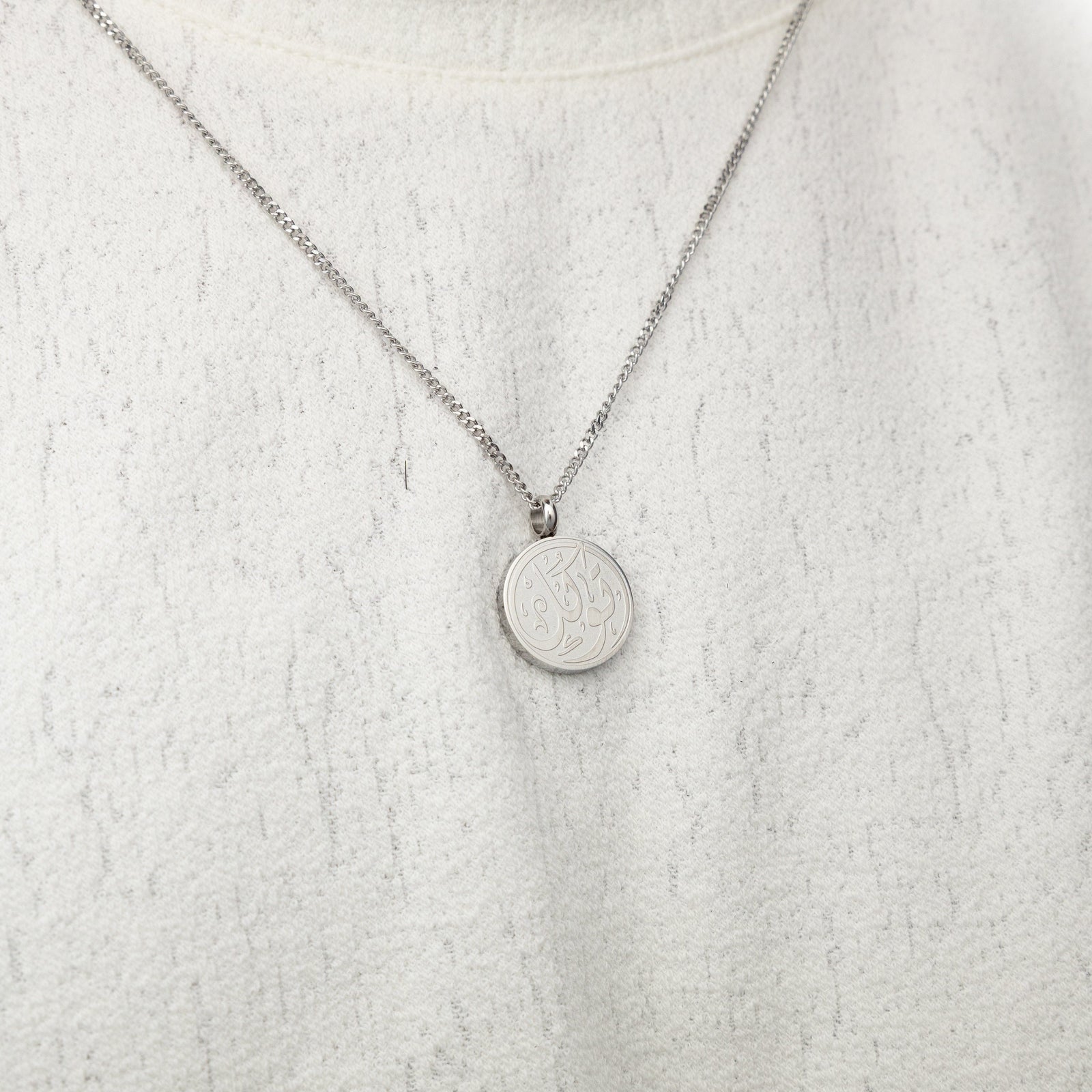 Silver trust token necklace worn on a textured white top.