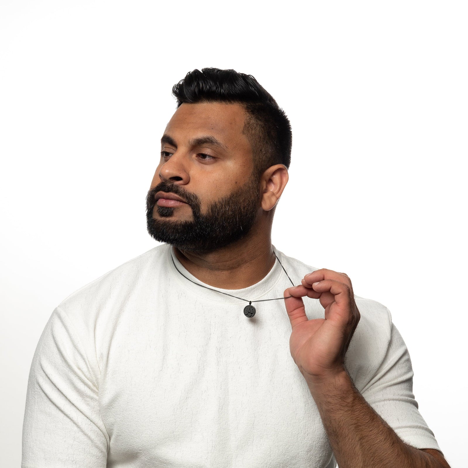 Man wearing a black trust token necklace, gently pulling the necklace, dressed in a white shirt.