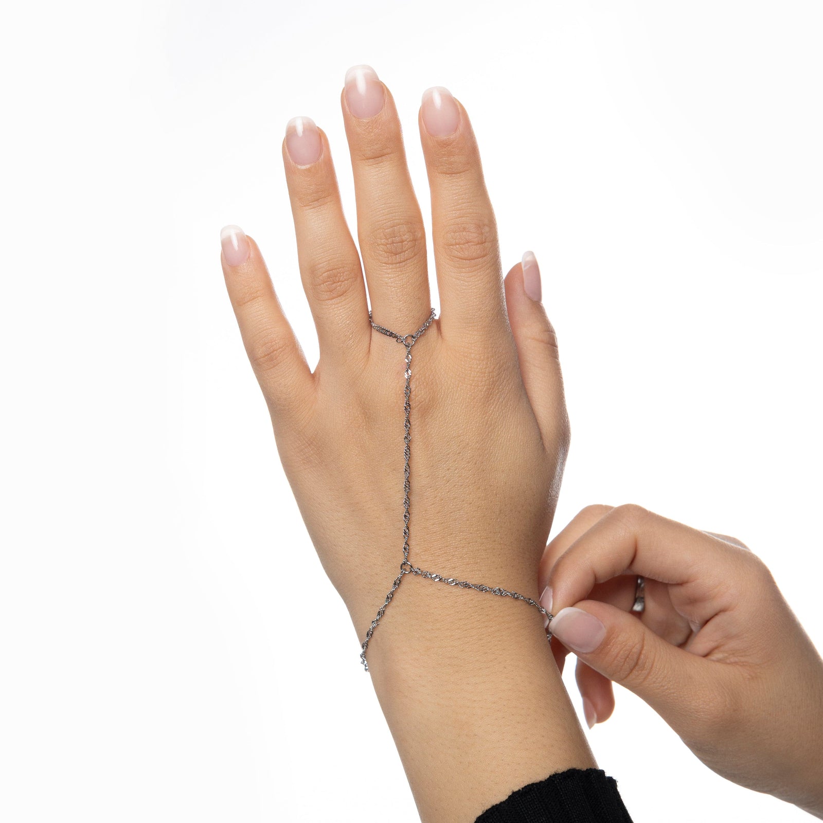 Close-up of a woman adjusting a silver twisted hand chain, ring loop fitted on middle finger, photographed on a clean white background.