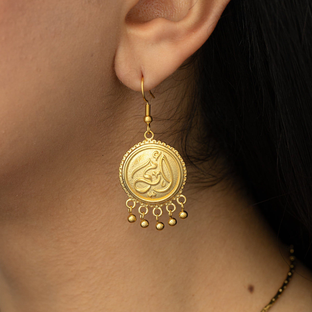 A pair of 18K gold plated dangling coin earrings that features "my mother" embossed in Arabic Calligraphy design finished with dancing orbs.