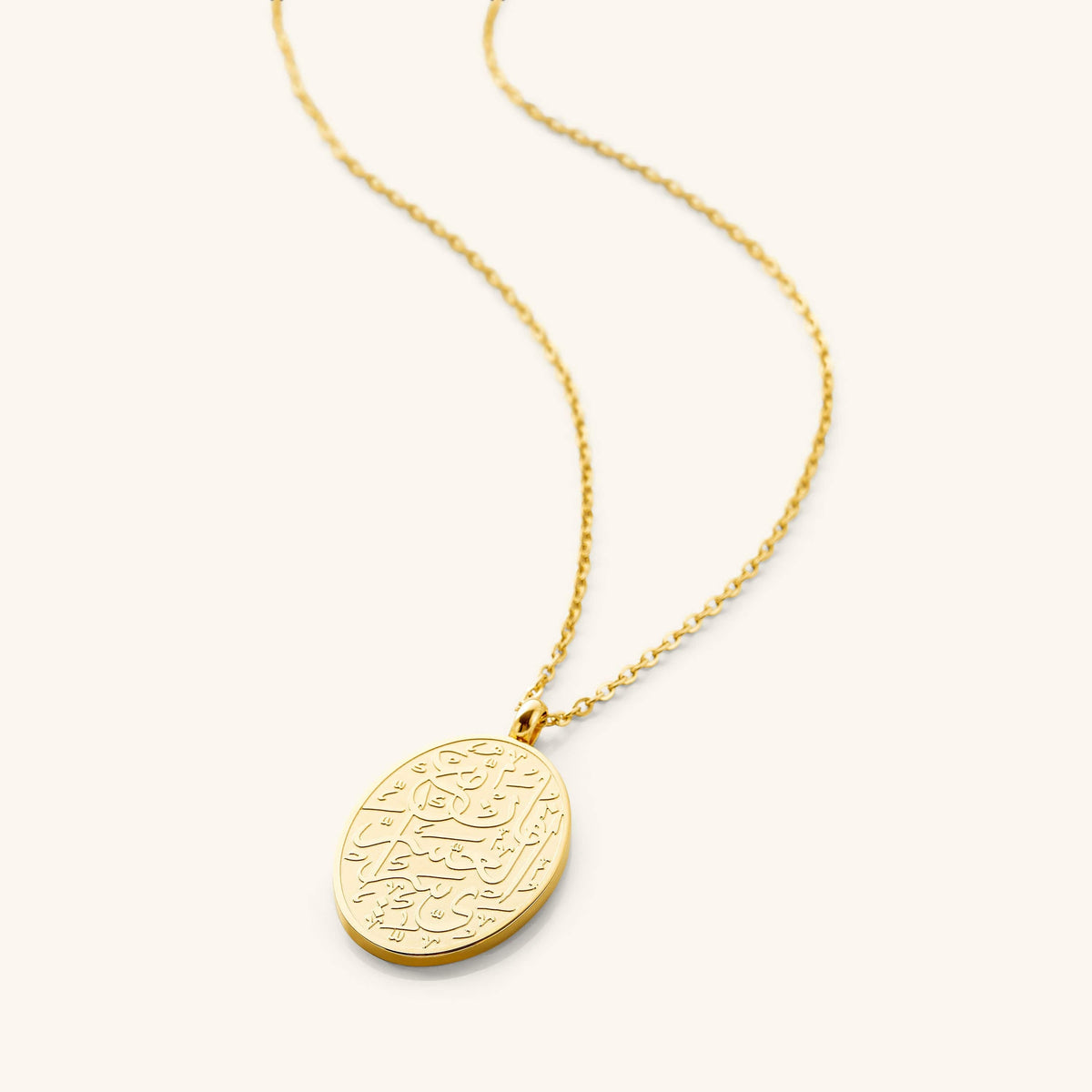 Flat lay of the 18k gold plated necklace that features an oval-shaped piece engraved with an inscription that means "with hardship comes ease" (94:5)