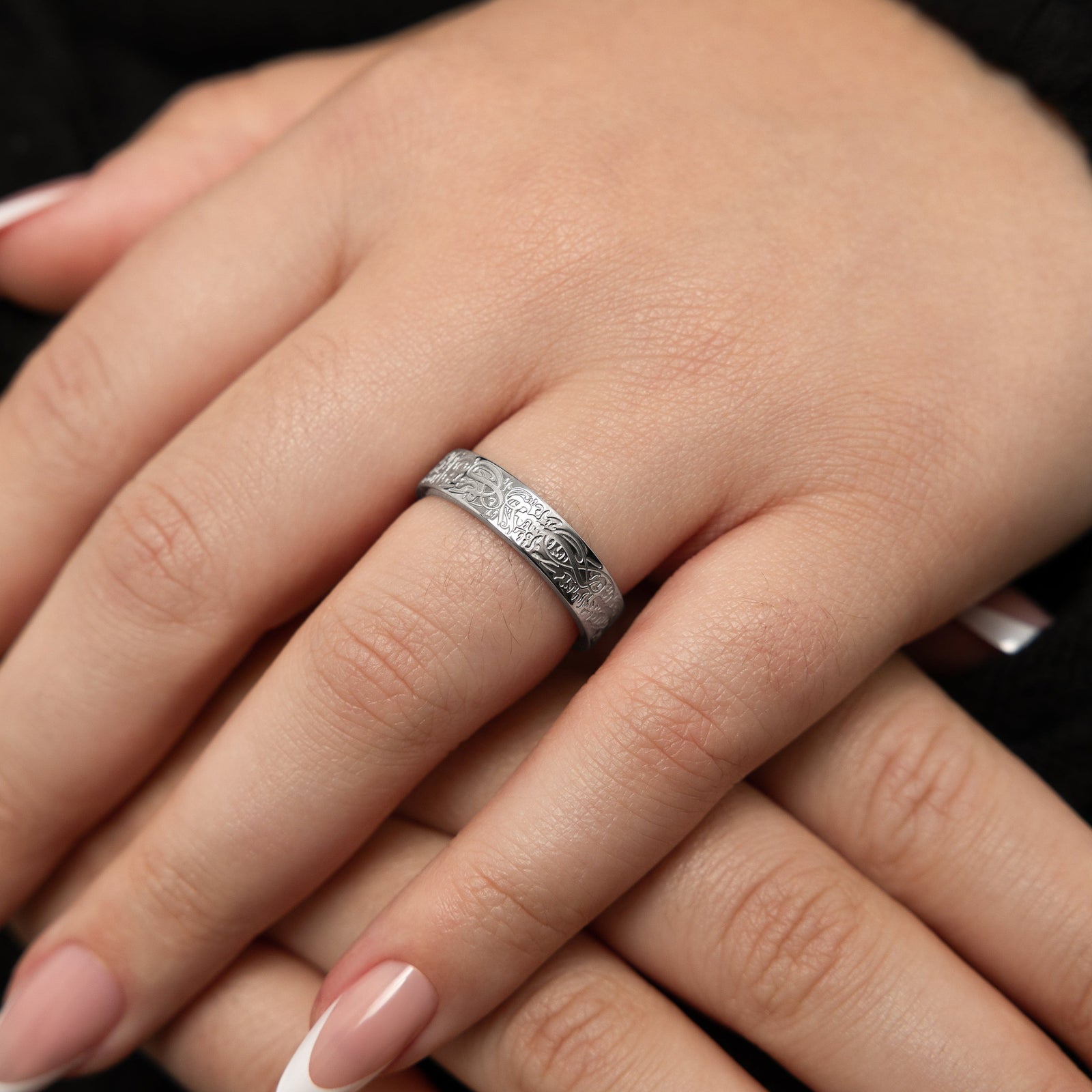 A close-up shot of a person's finger wearing a silver With Hardship Comes Ease Ring V2.