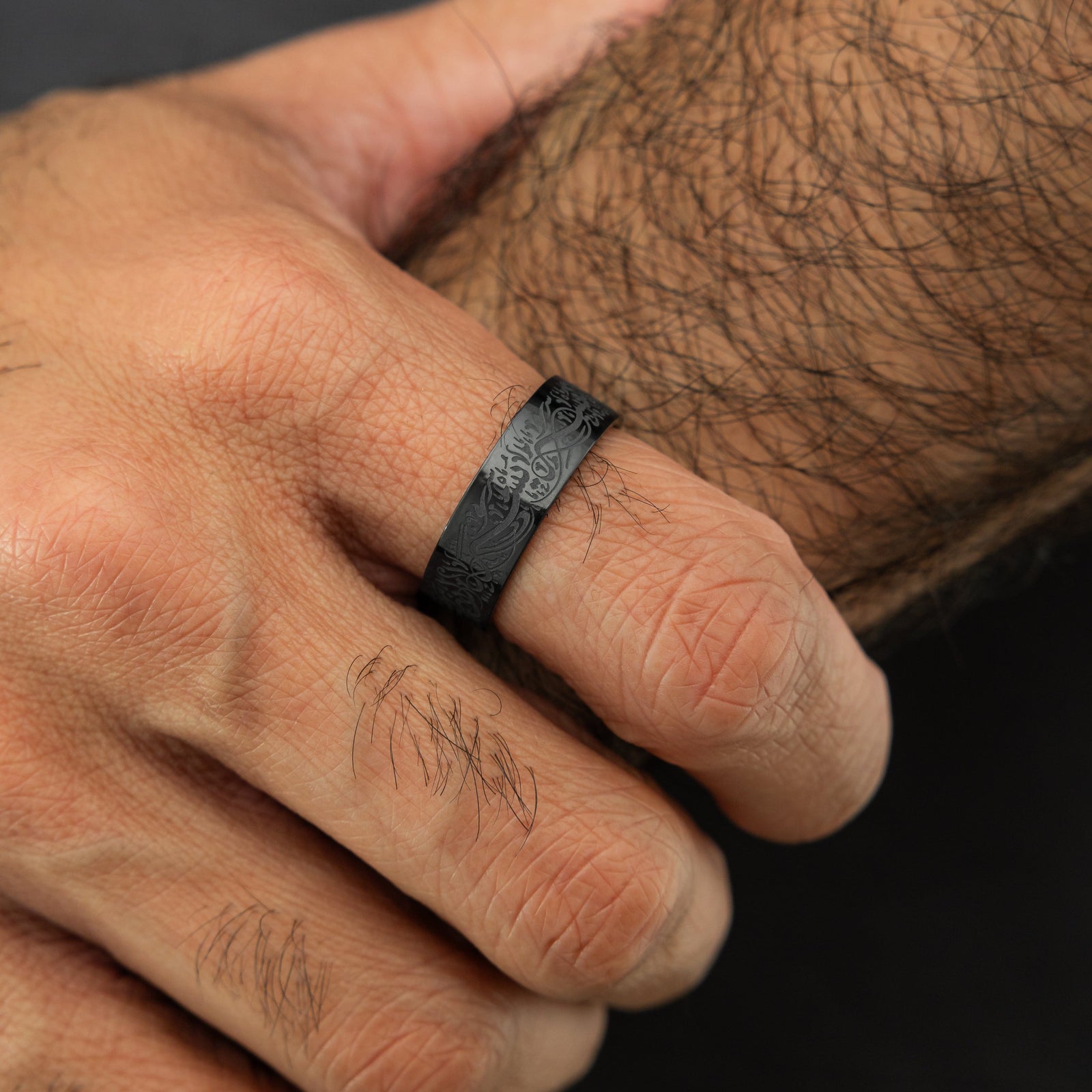 Close up of the black "With Hardship Comes Ease" Ring V2 | Men as worn by the model on their right index finger.