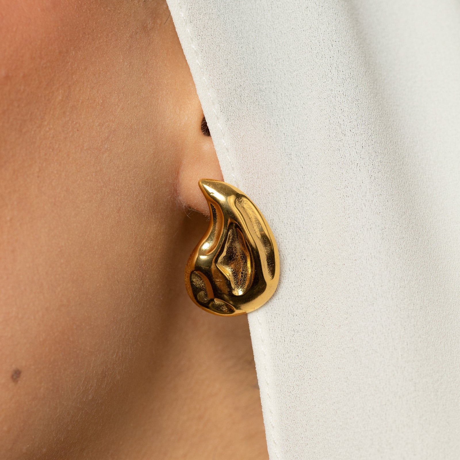 Gold vintage droplet earring worn by a person with a white headscarf