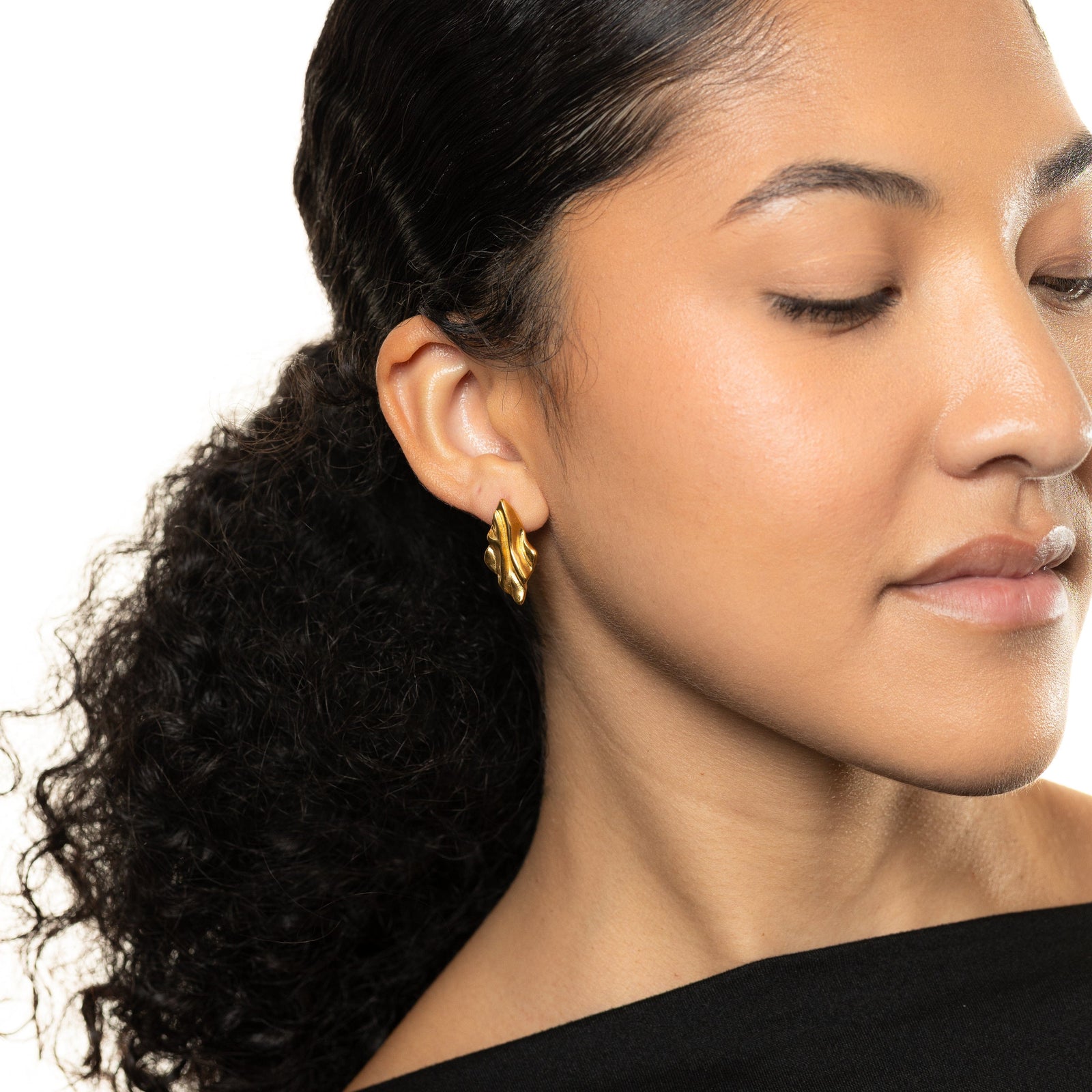 a woman wearing gold vintage meldted earrings with a neutral background