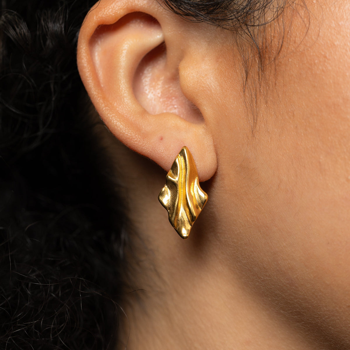 Gold vintage melted earring worn on an ear 