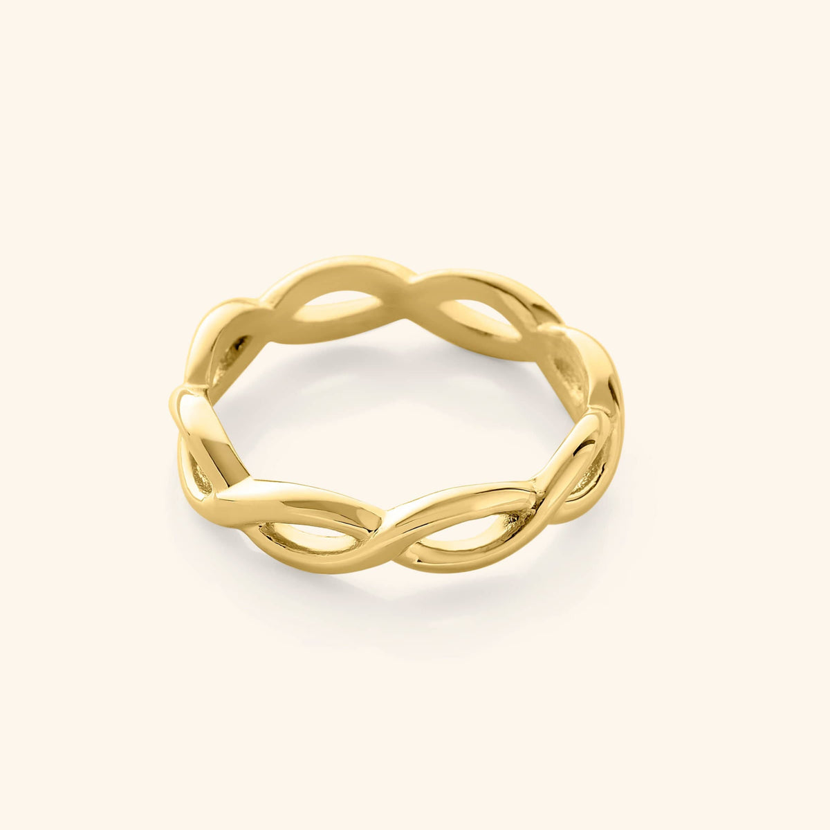 Gold infinity ring with a continuous twisted loop design, photographed against a neutral beige background.