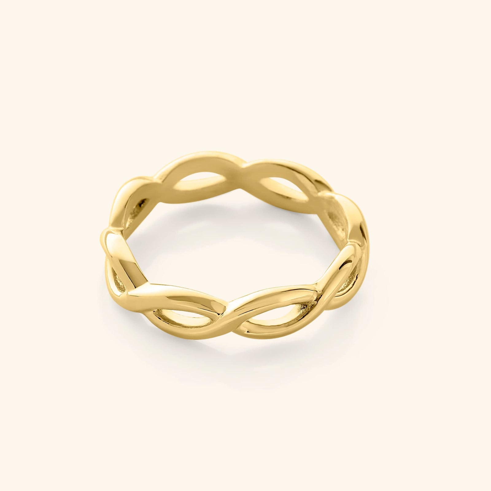Gold infinity ring with a continuous twisted loop design, photographed against a neutral beige background.