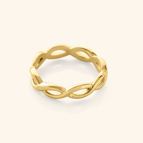 Gold infinity ring with a continuous twisted loop design, photographed against a neutral beige background.