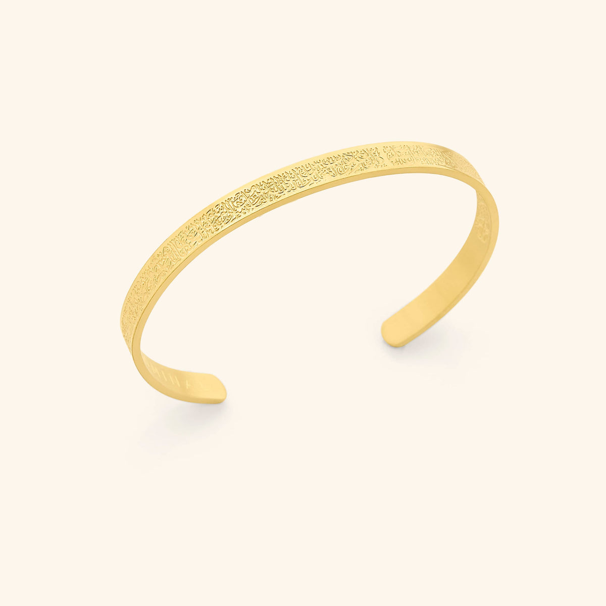 Photo of the 18k gold plated 4 Qul Cuff against a light background.This piece features the four surahs beginning with "Qul" separated with a slight gap on the cuff, engraved on the front and back.