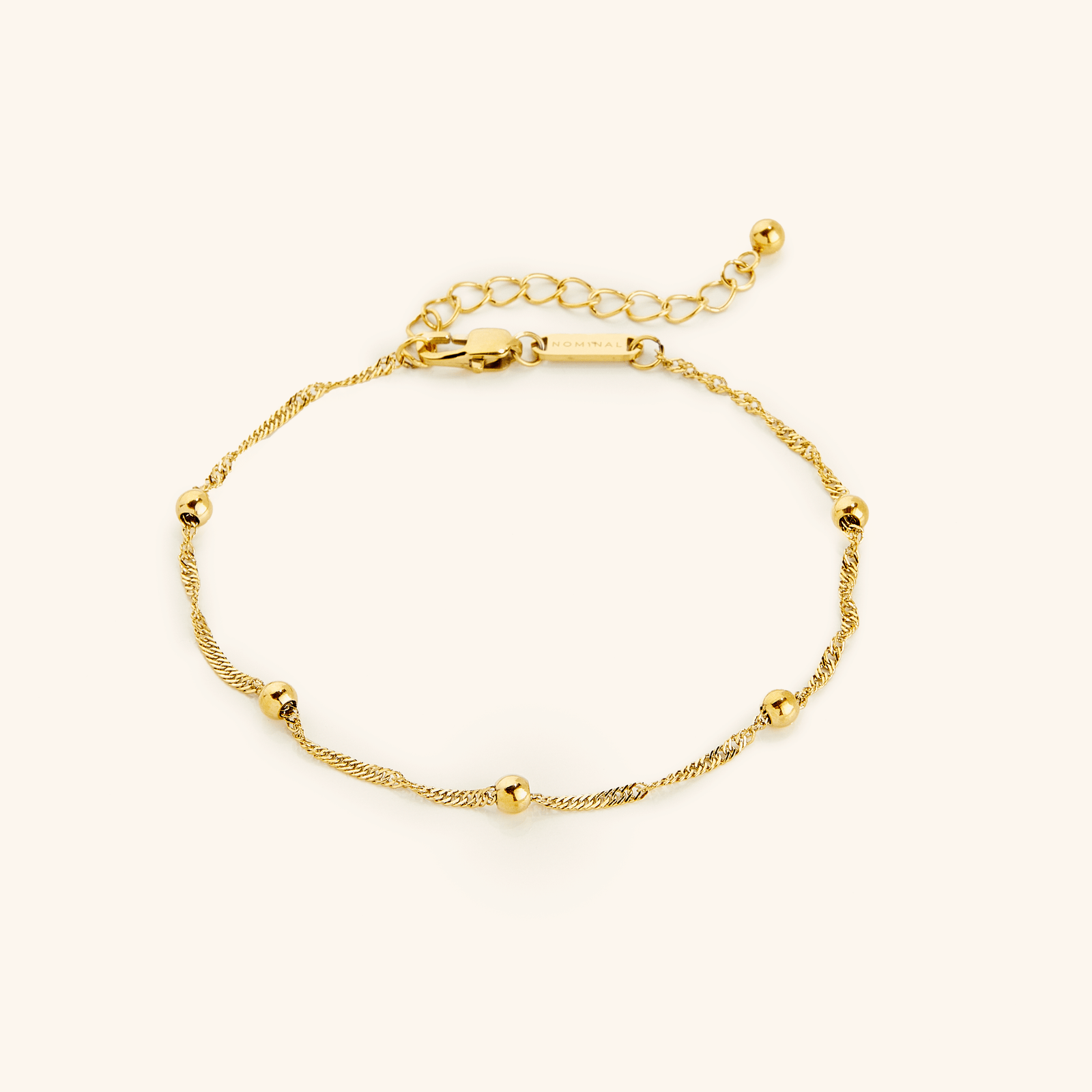 Flat lay of an 18k gold plated bracelet. The Dotted Twisted Anklet features twisted chain and dotted orbs.