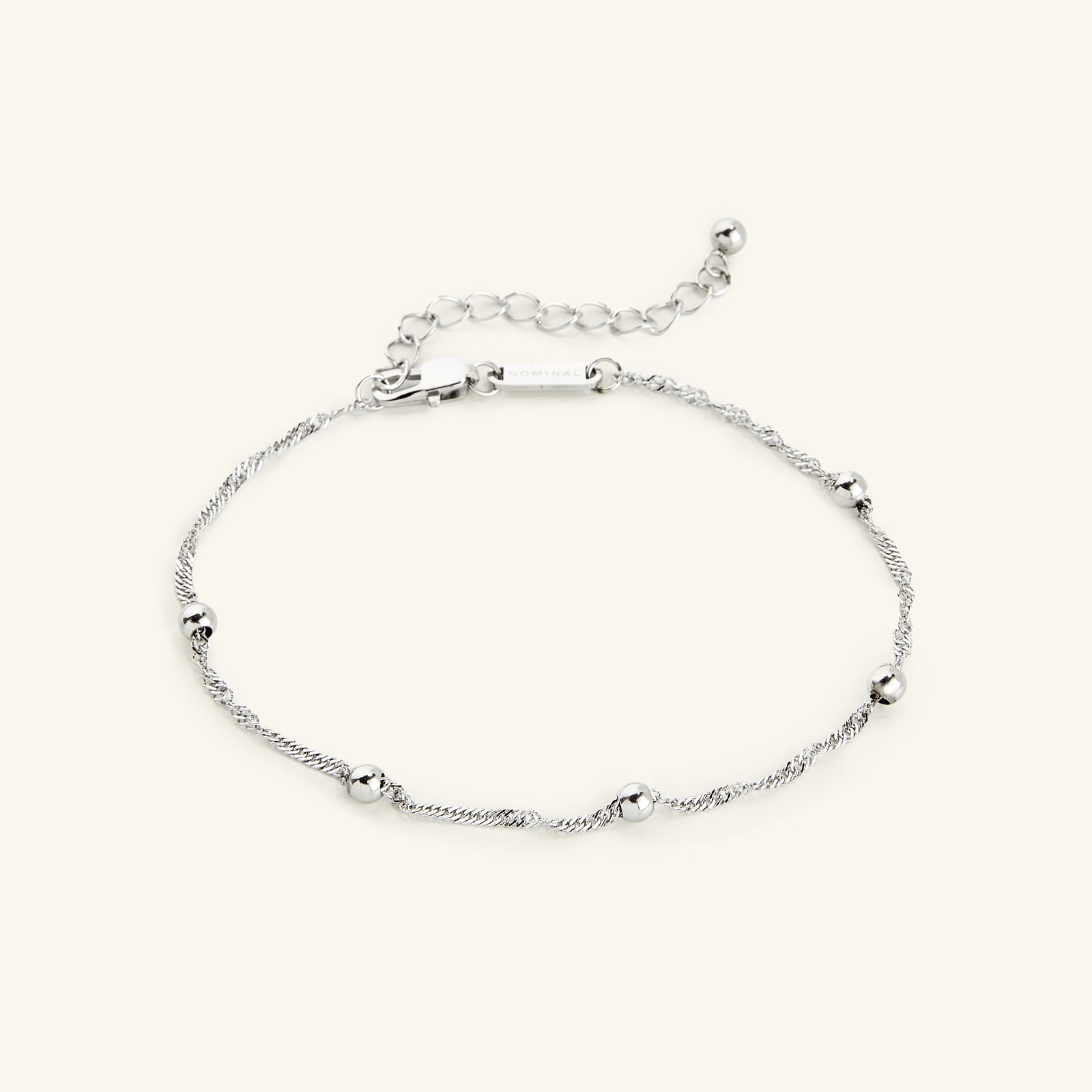 Flat lay of a silver bracelet. The Dotted Twisted Anklet features twisted chain and dotted orbs.