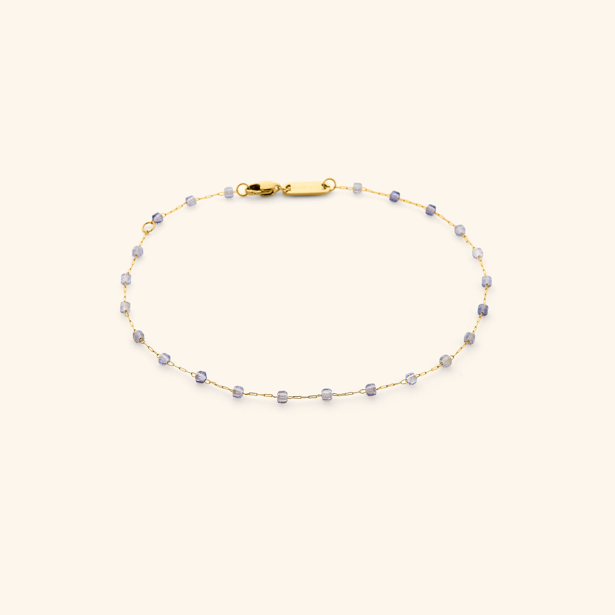 The Essential Iolite Micro Anklet featuring an 18k gold-plated dainty chain accented with faceted violet-blue iolite beads and secured with a lobster clasp, shown on an off-white background.