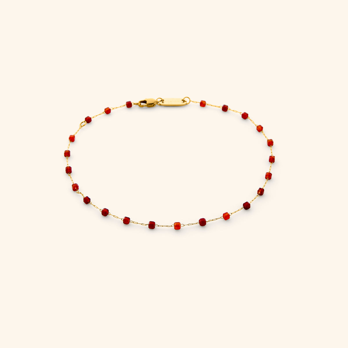 The Essential Micro Anklet featuring an 18k gold-plated dainty chain accented with faceted vibrant red gemstone beads and secured with a lobster clasp, shown on an off-white background.