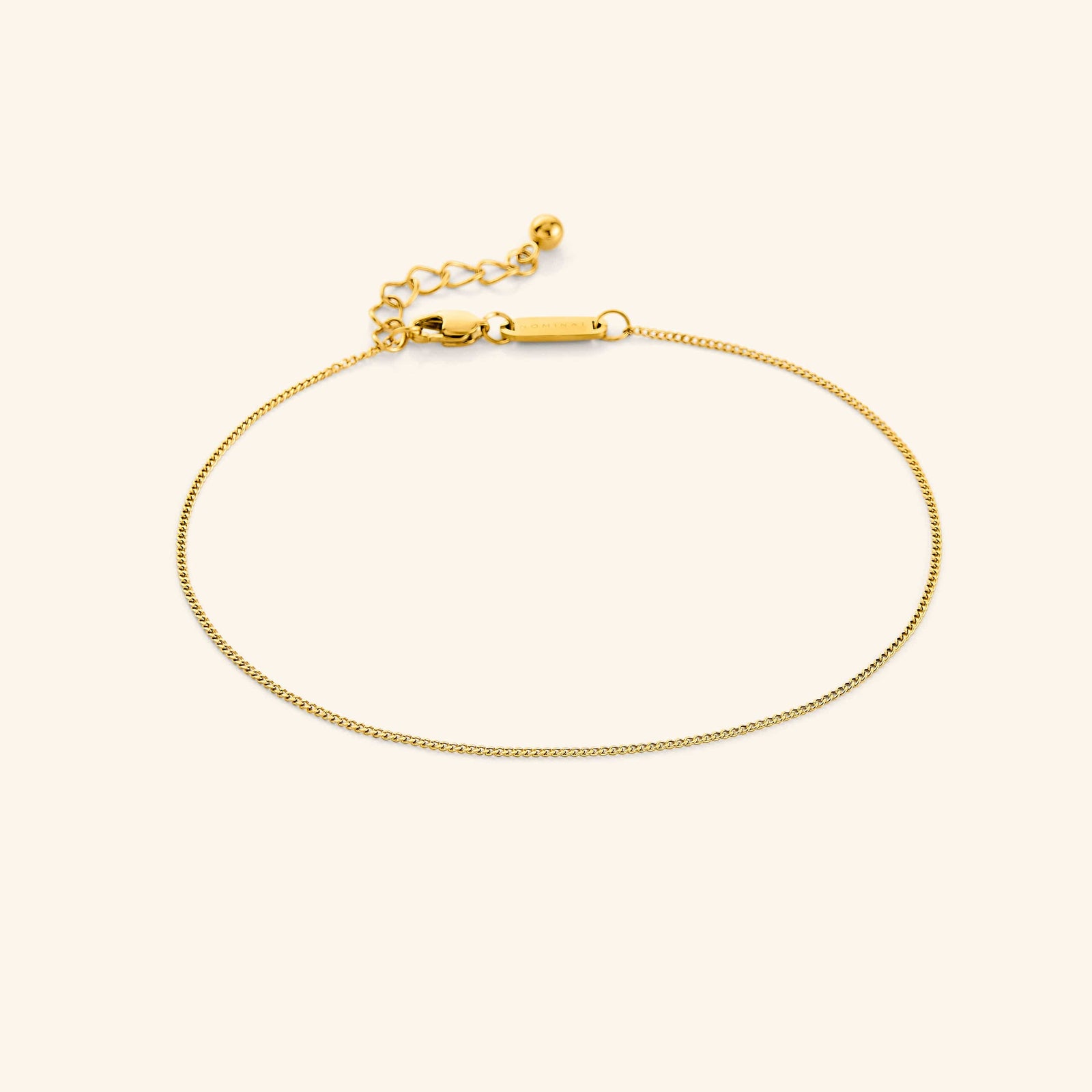 Photo of the 18k gold plated Micro Curb Anklet against a light background. This anklet features a 1MM flat oval chain pattern