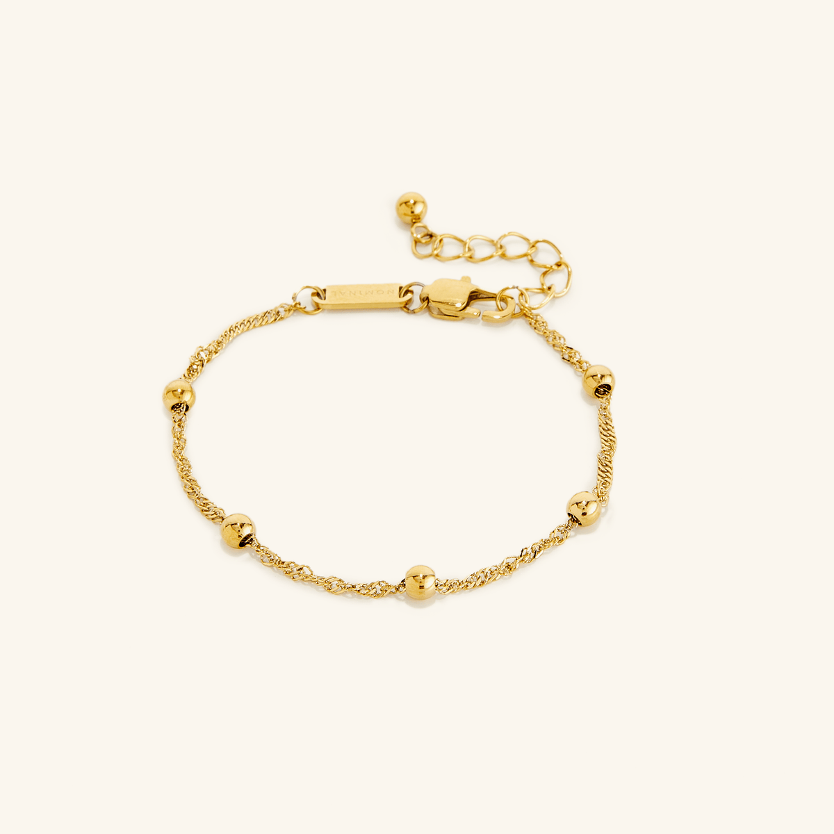 Flat lay of an 18k gold plated bracelet. The Dotted Twisted Bracelet features a spiraling chain that brings gorgeous dotted beads together for the perfect touch.