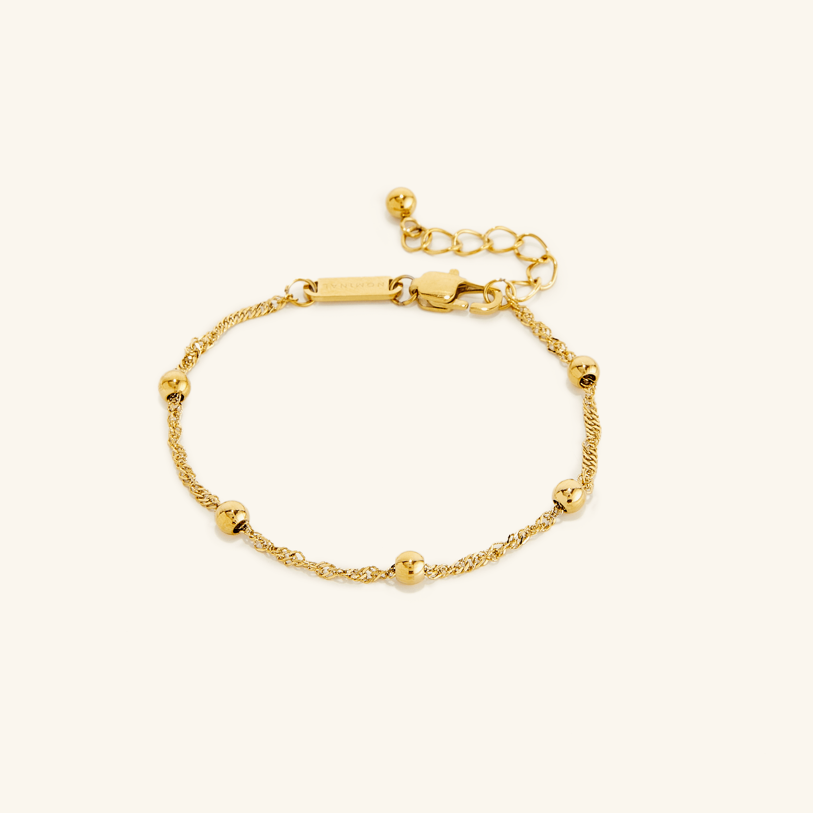 Flat lay of an 18k gold plated bracelet. The Dotted Twisted Bracelet features a spiraling chain that brings gorgeous dotted beads together for the perfect touch.