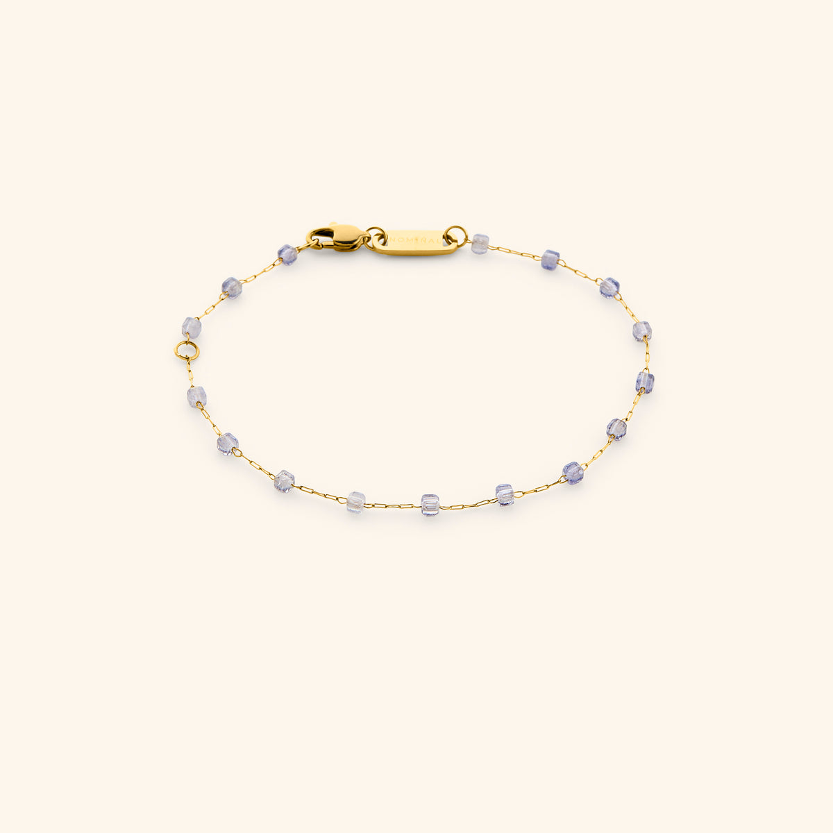 The Essential Iolite Micro Bracelet by Nominal, featuring a delicate 18k gold-plated chain accented with soft violet-blue beads and secured with a lobster clasp on an off-white background.
