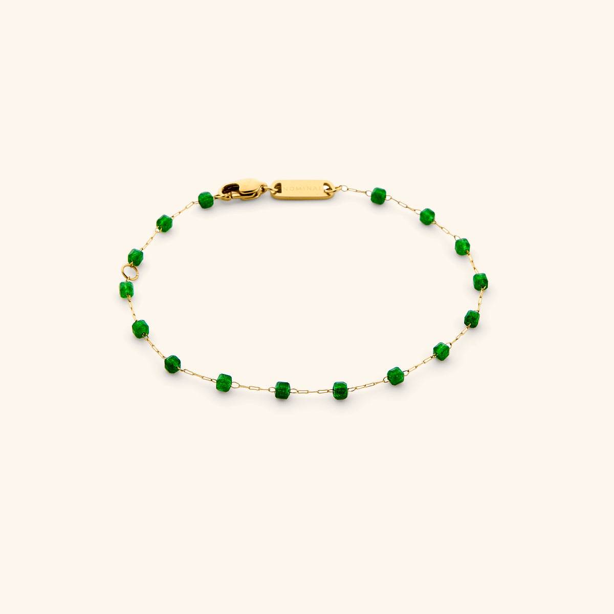 18k gold-plated micro anklet with vibrant green emerald beads laid out on a soft light background.
